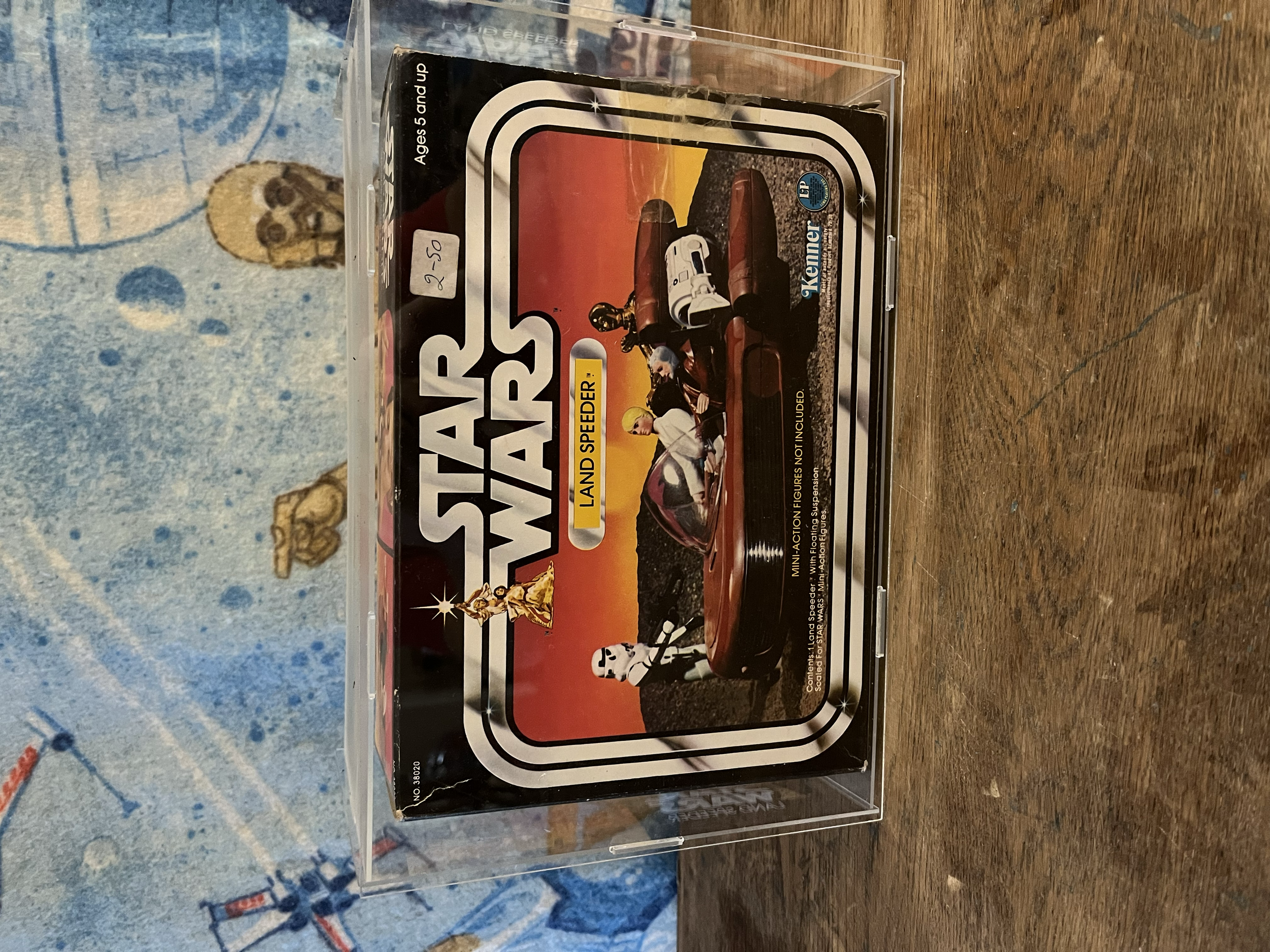 Star Wars Landspeeder miniature model in clear display case on a wooden surface, with a blue patterned fabric in the background.