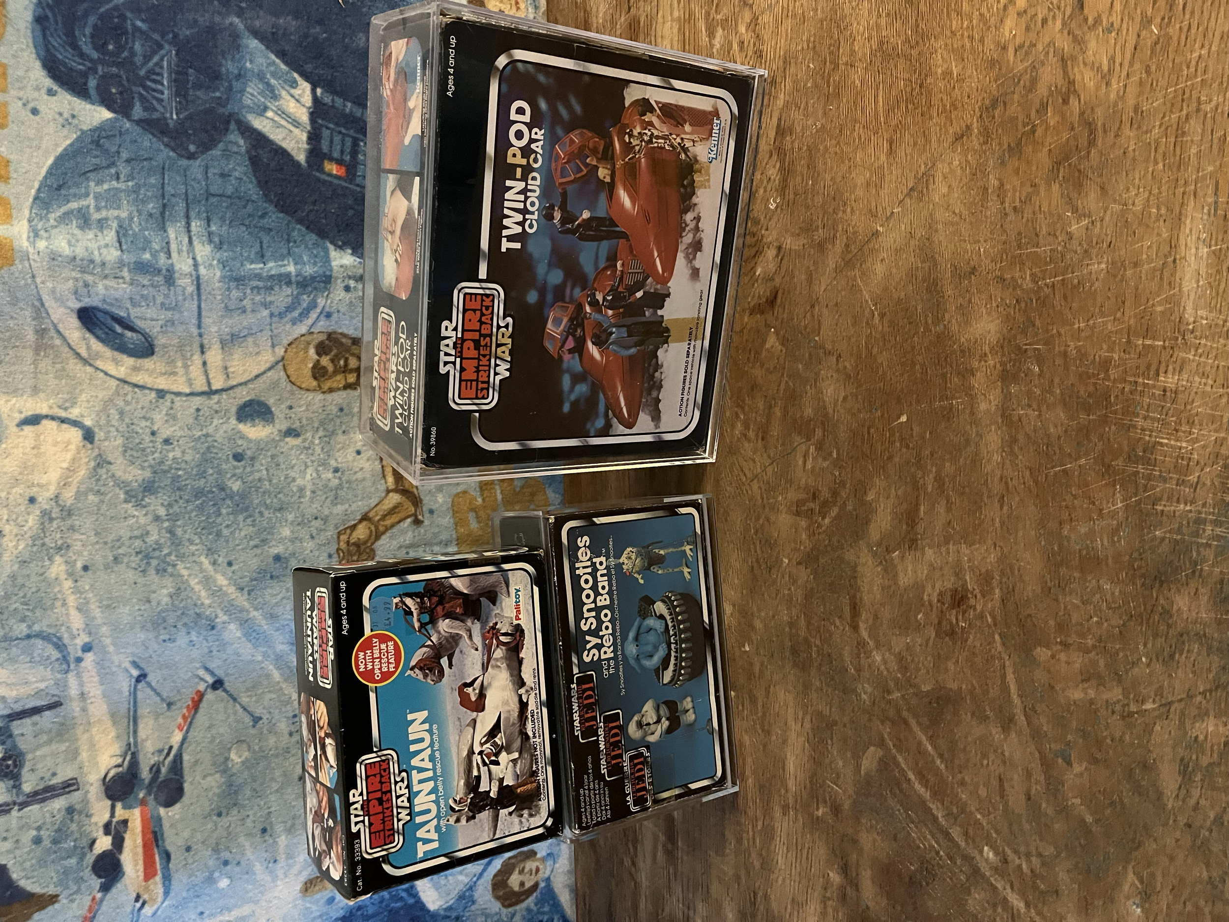 Star Wars The Empire Strikes Back Taun Taun and Rebel Speeder toy packaging box on a wooden surface with a blue patterned background.
