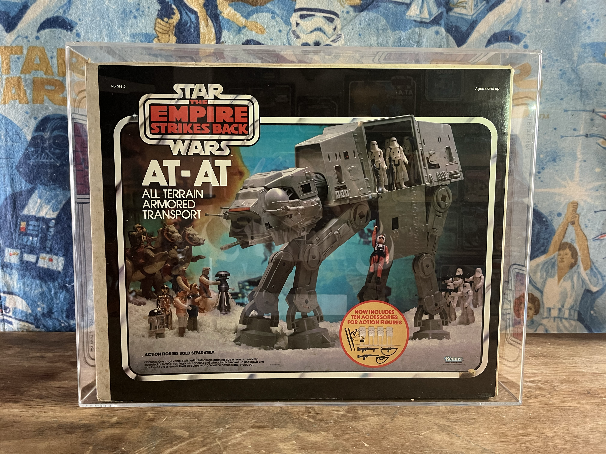 Star Wars The Empire Strikes Back AT-AT all terrain armored transport toy package, featuring a grey AT-AT walker with action figures around it, set against a blue and orange background with textures and partially visible characters.