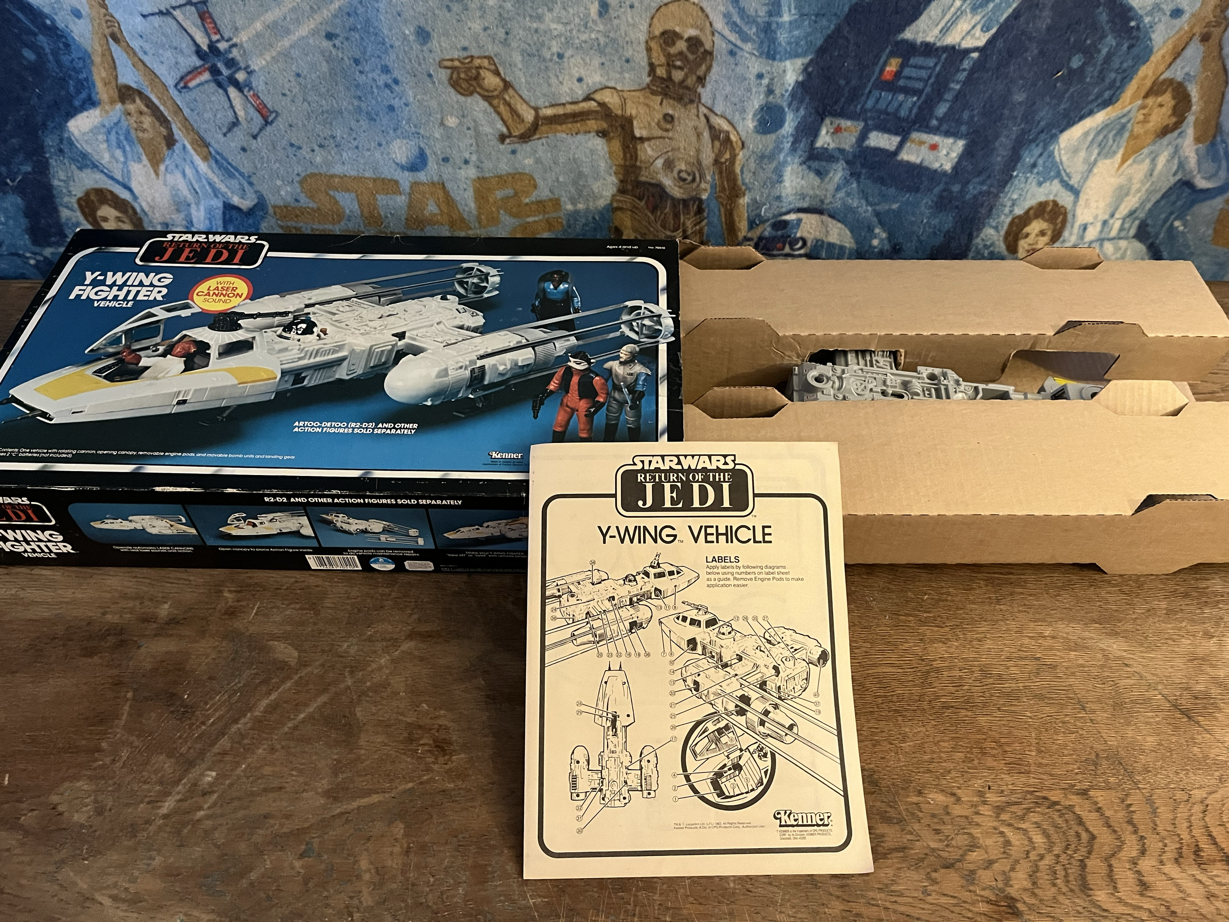 A model spaceship from the Star Wars Return of the Jedi series on top of an instruction manual, with a Star Wars-themed mural in the background.