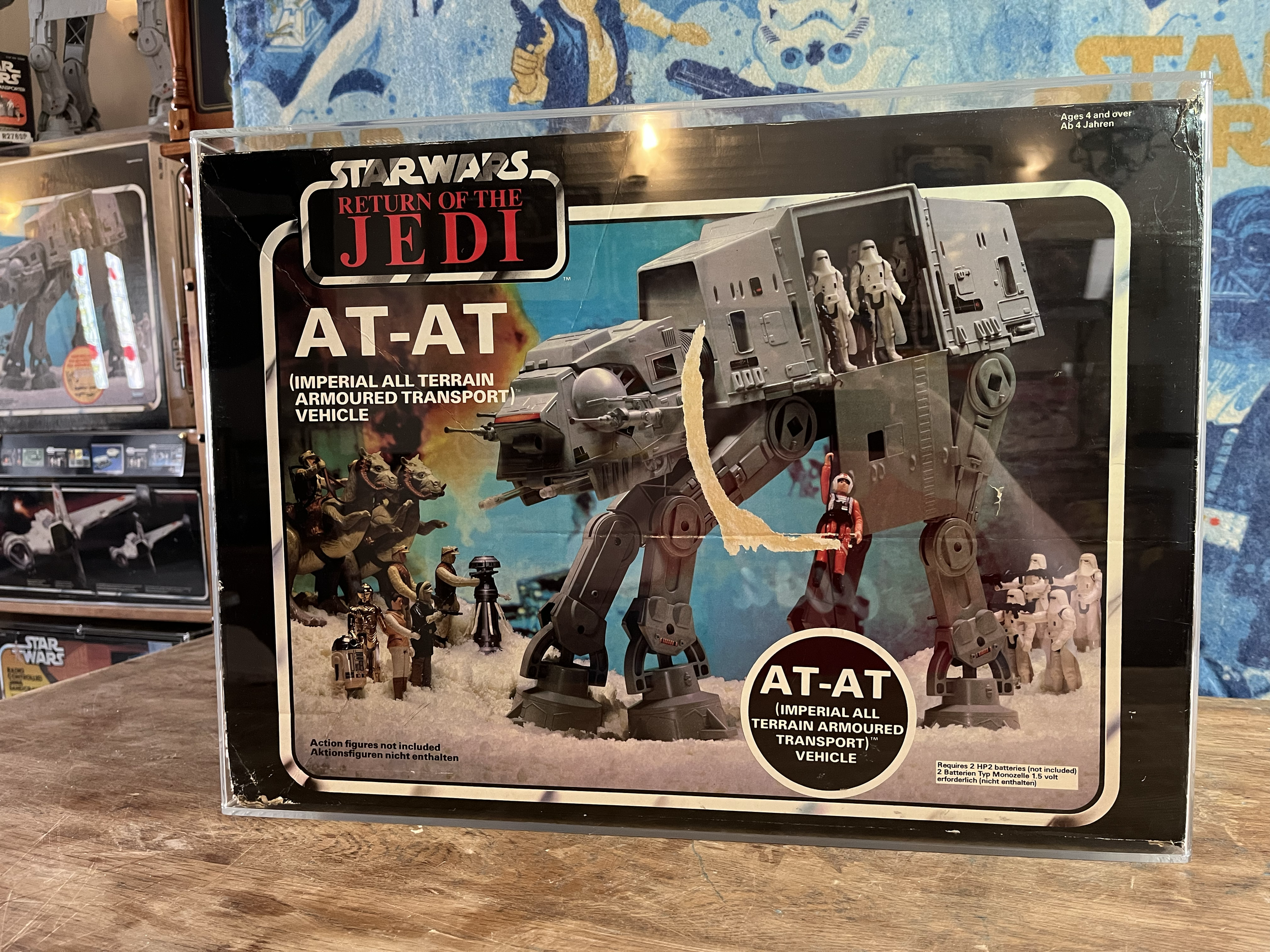 Star Wars Return of the Jedi AT-AT Imperial All Terrain Armoured Transport Vehicle toy box with image of a large gray toy vehicle and figures of soldiers and animals set against a space scene with explosions, and various other boxes of toys in the ba