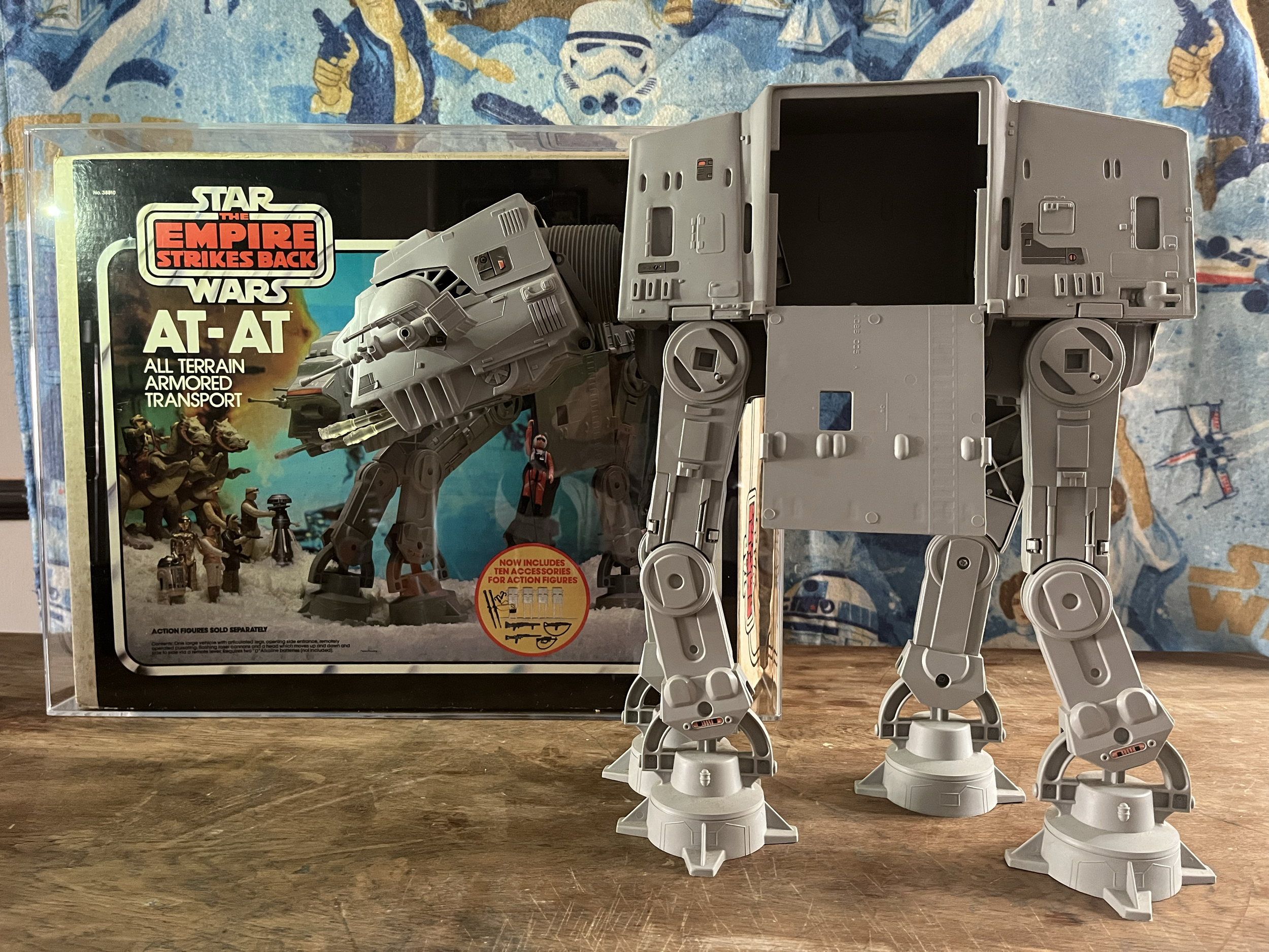 Model of AT-AT Walker from Star Wars, placed on a wooden surface with Star Wars merchandise box and a star wars-themed blanket in the background.