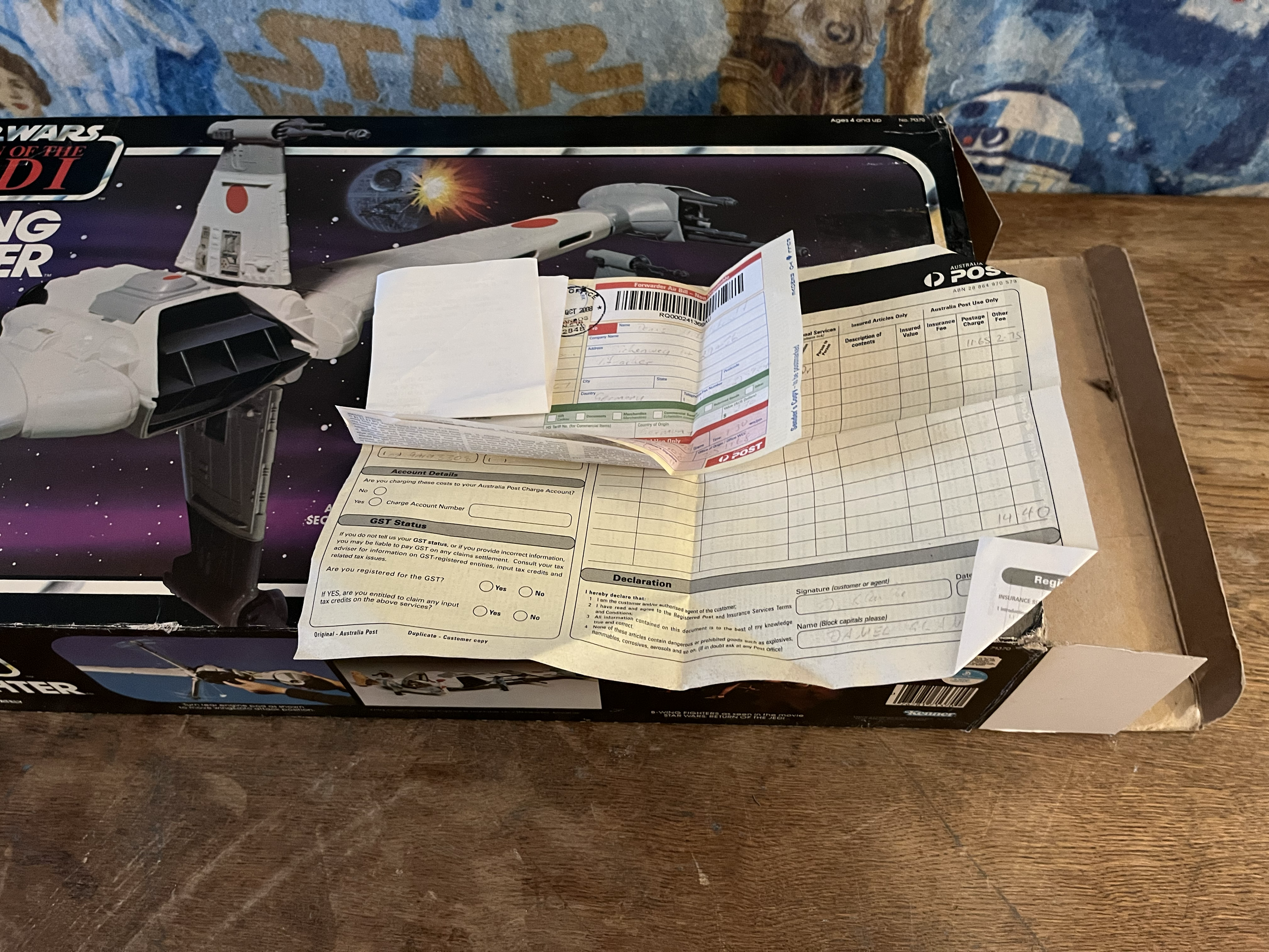 A box of Star Wars action figures featuring the Starfighter from the Star Wars series, with Japanese writing and space-themed artwork on the packaging. There are also some papers, including a post payment form and a handwritten note, on top of the bo