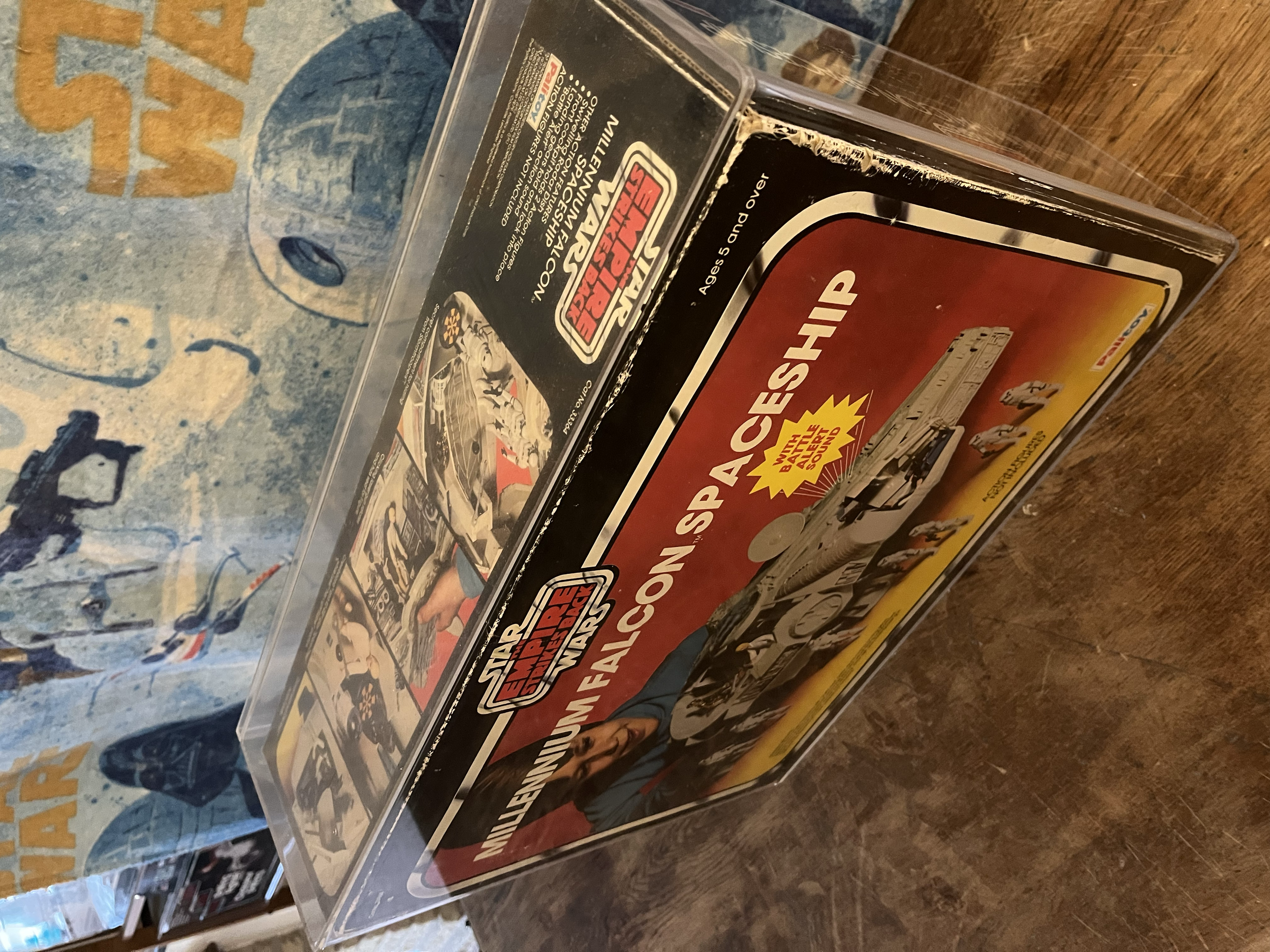 A sealed plastic case containing a vintage Star Wars Darth Vader toy or collectible, with a colorful artwork background and part of a Star Wars branding label visible.