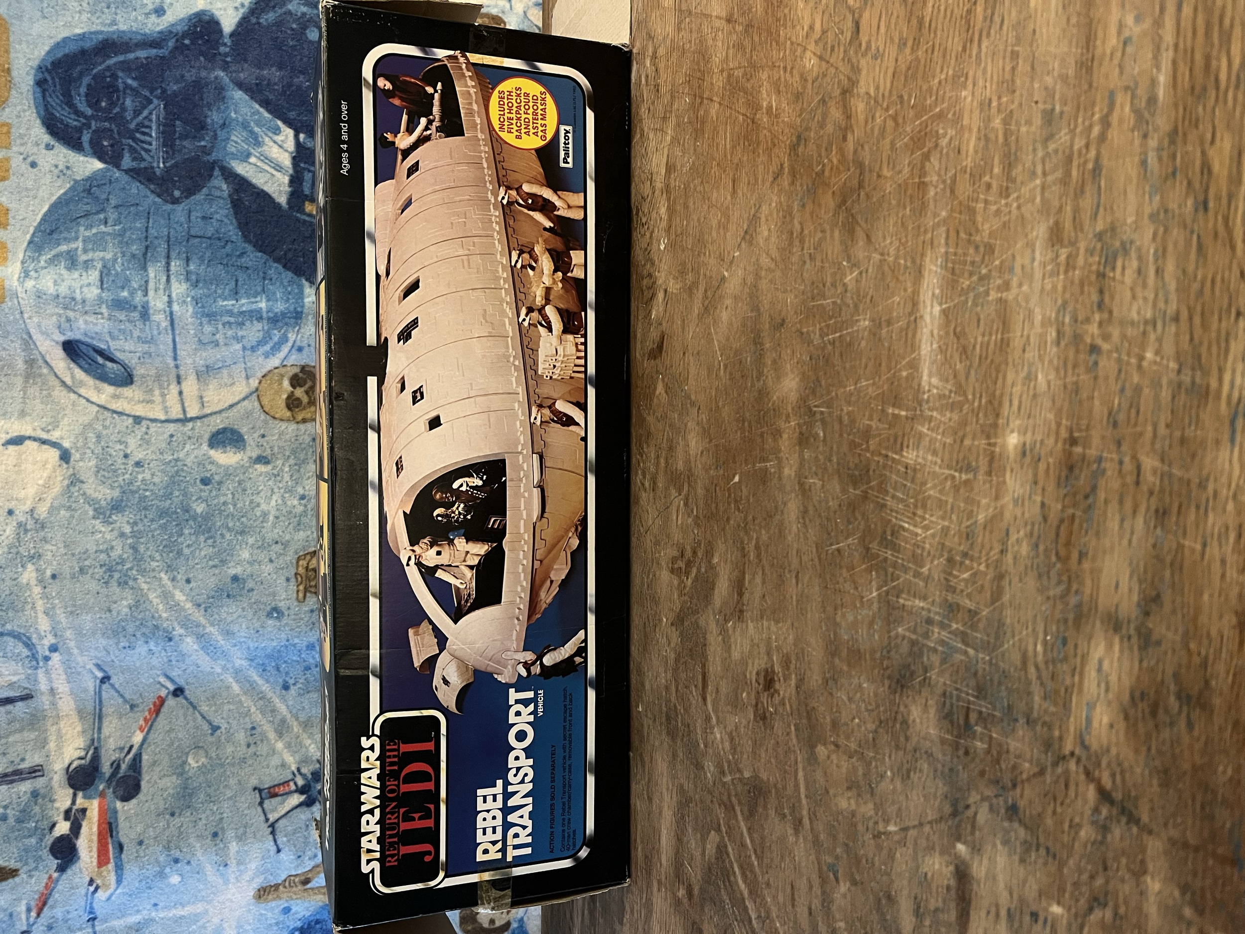 A boxed toy set of the Millennium Falcon spaceship from Star Wars with action figures inside, on a wooden surface.