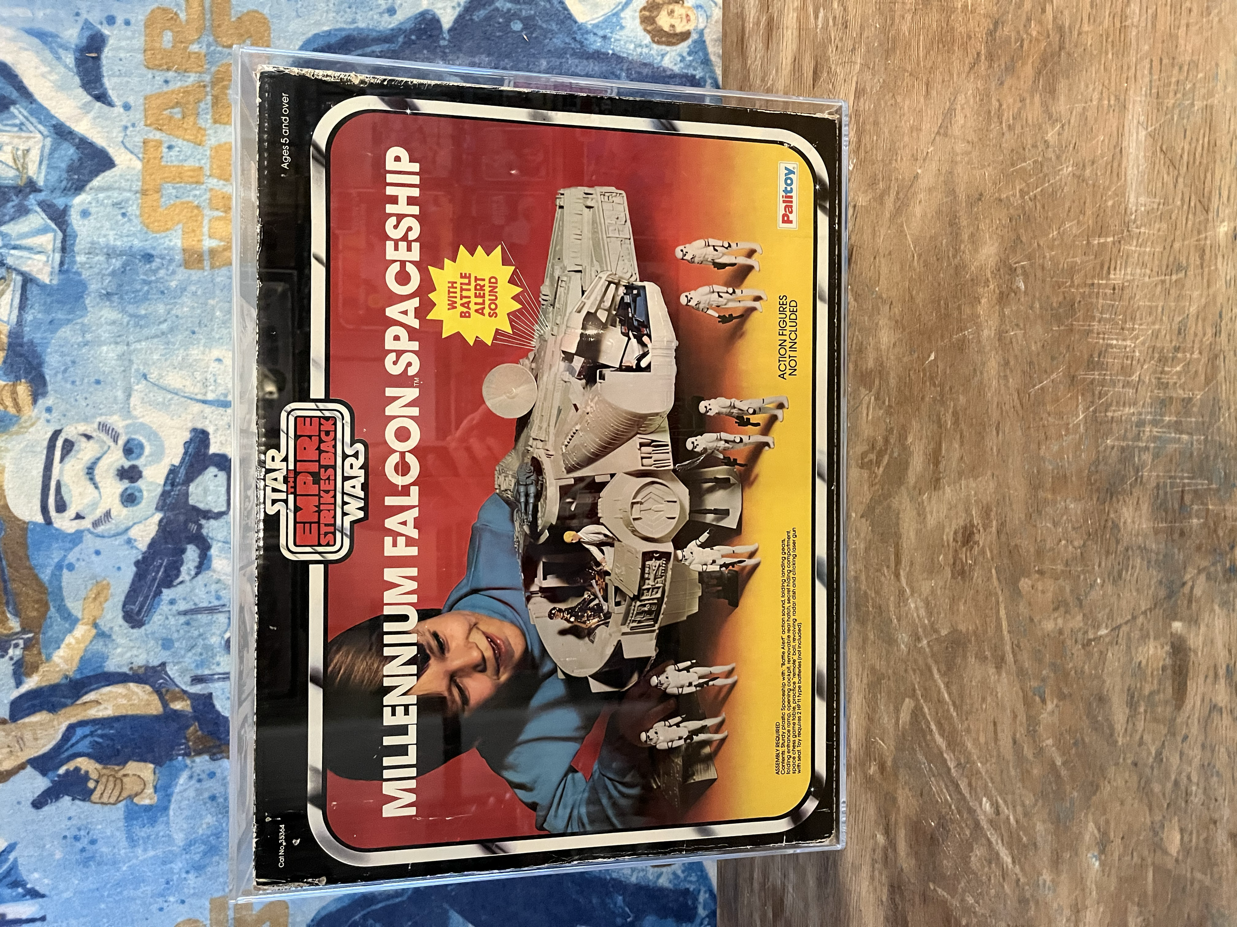 Star Wars Millennium Falcon action figure package with Stormtroopers and other characters, in plastic case on wooden surface.