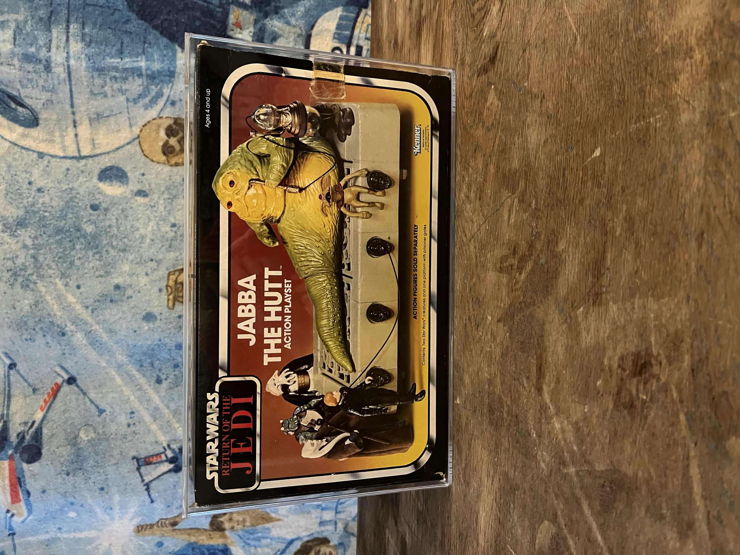 Action figures from Star Wars on a plastic case, with a background of a blue wall and a wooden surface.