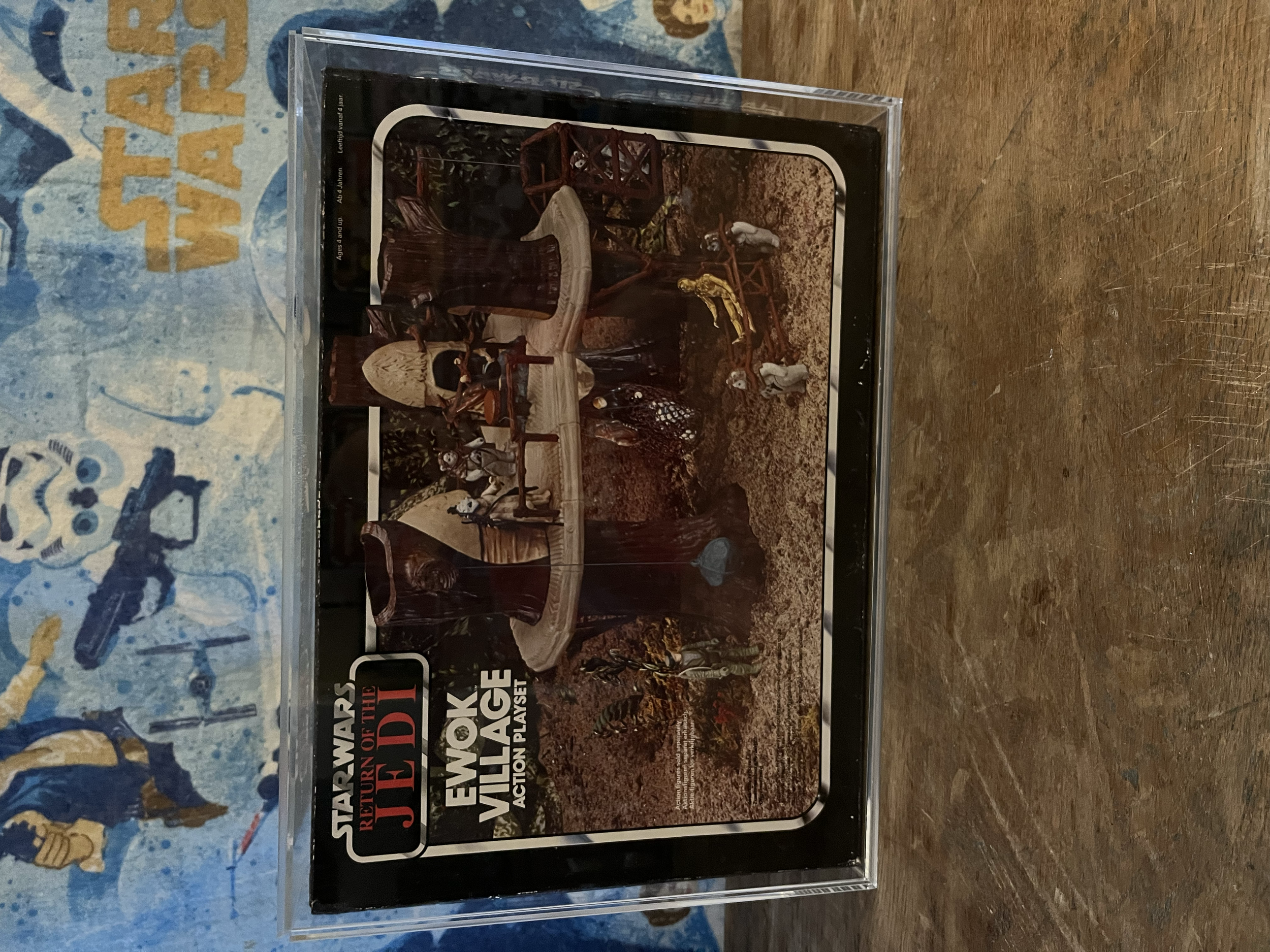Close-up of a tabletop game box for 'Warriors of the Jacobin' with artwork of a forest scene and a group of soldiers, next to a blue cloth with yellow and navy designs.