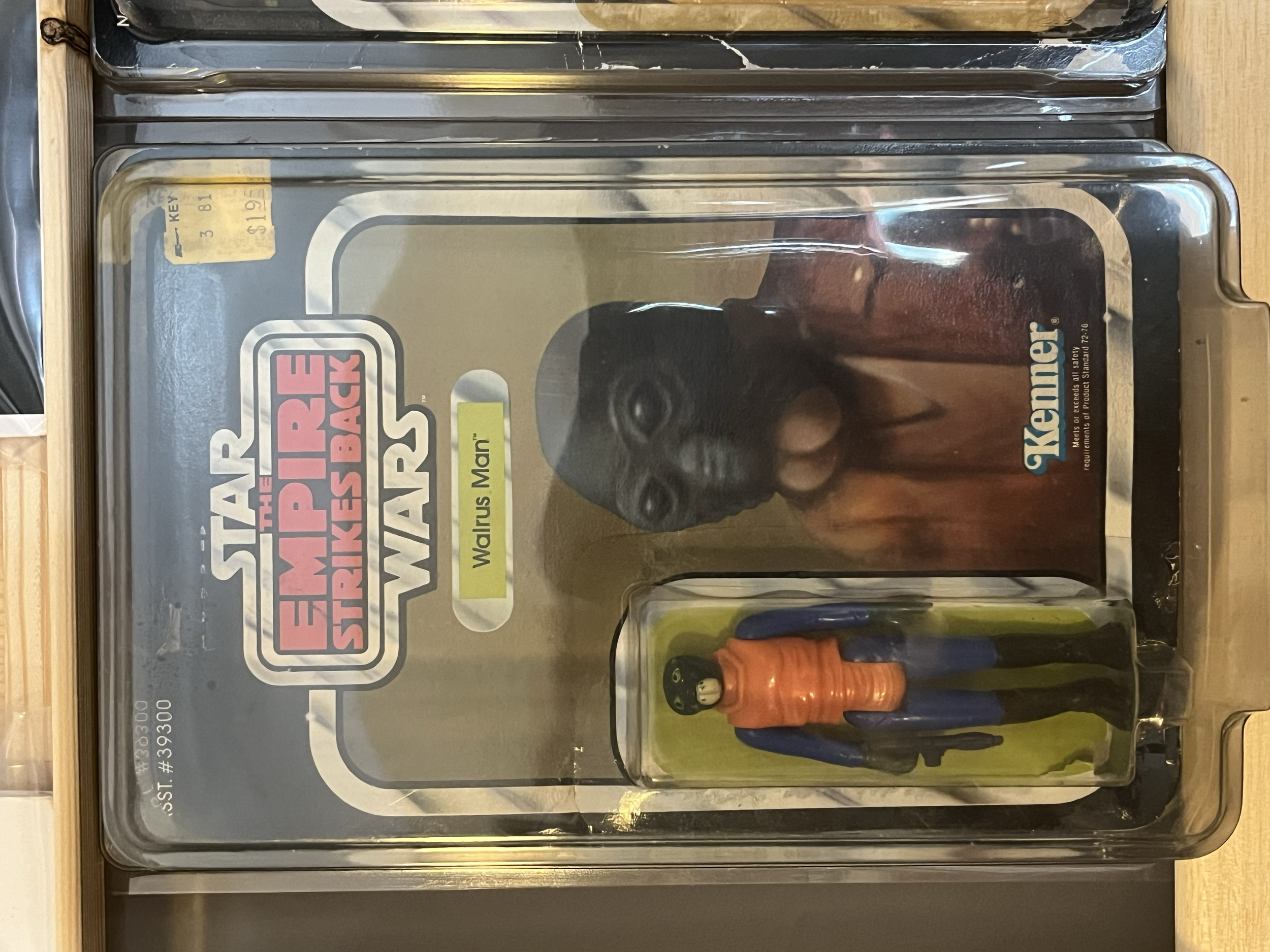 A Shadow Stormtrooper action figure with a black helmet and an orange jumpsuit attached to a backpack, displayed in a glass case with a Star Wars The Empire Strikes Back logo sticker on the front.