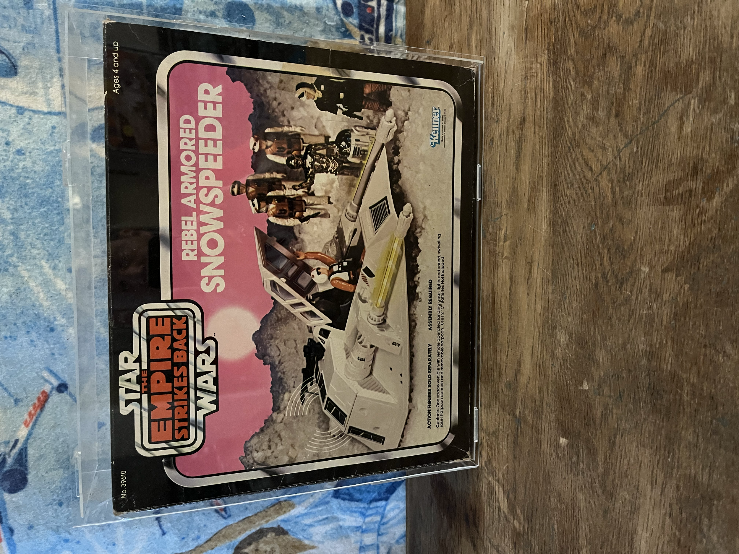 A sealed vintage 'Star Wars' action figure set called 'Emperor Rebel Stormtrooper' in plastic packaging, with a label portraying characters and scenes from the Star Wars universe, placed on a wooden surface.