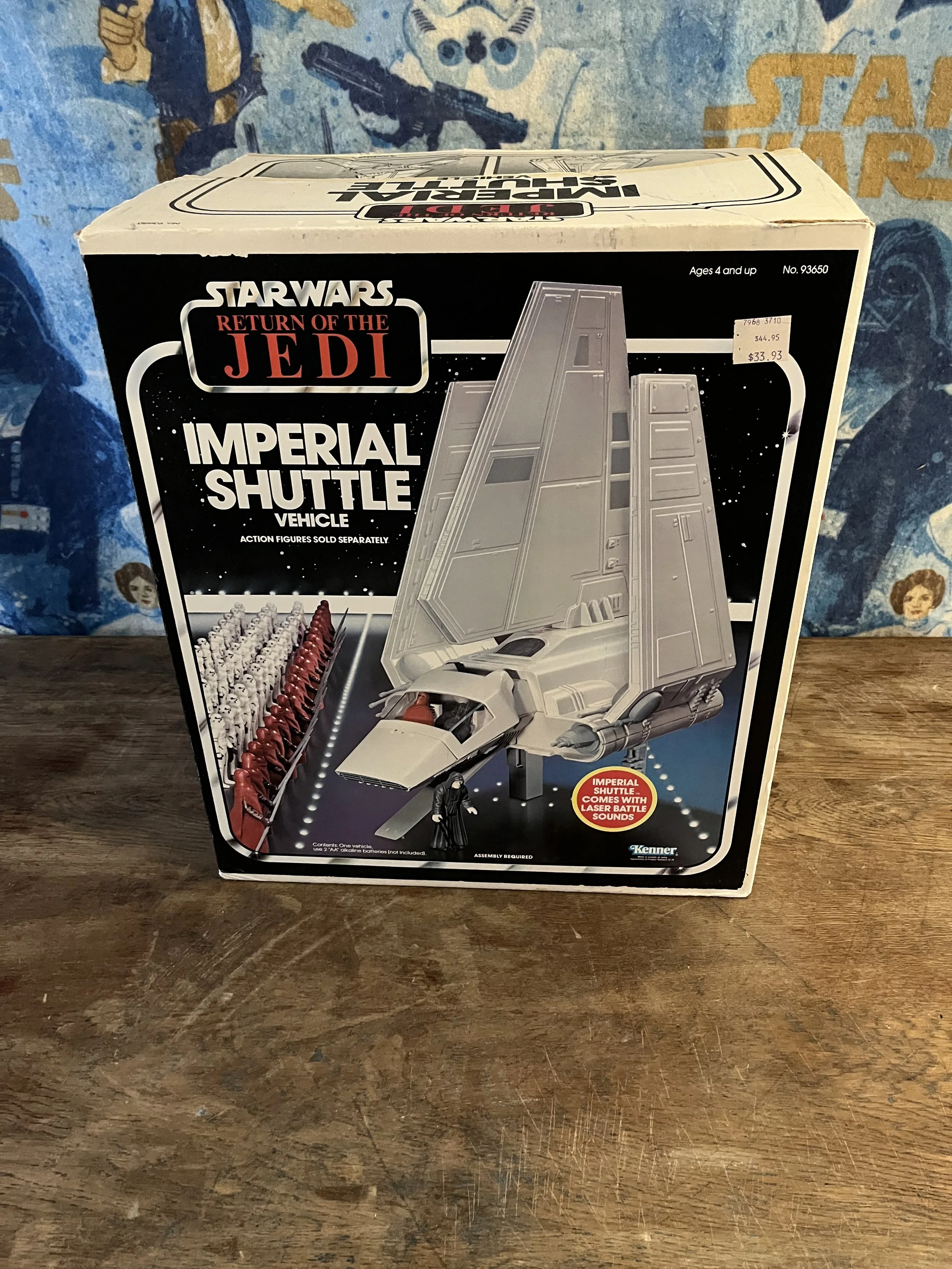 Star Wars Return of the Jedi Imperial Shuttle toy box with a picture of a spaceship and Darth Vader figure, placed on a wooden surface with a Star Wars themed background.