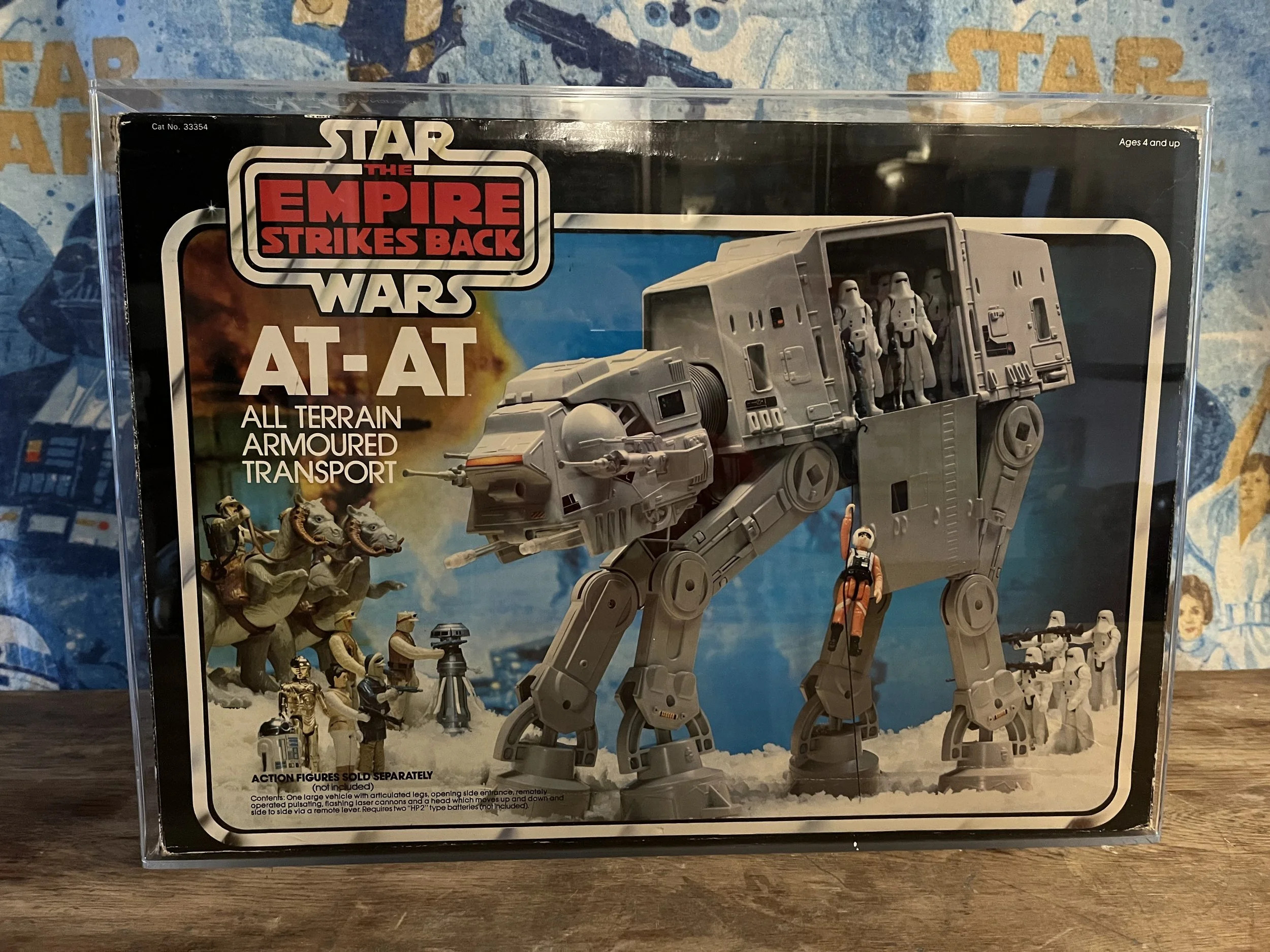 Packaging for a Star Wars The Empire Strikes Back AT-AT toy with an image of the all-terrain armored transport vehicle, featuring stormtroopers and other Star Wars characters and vehicles on a desert-like landscape background.