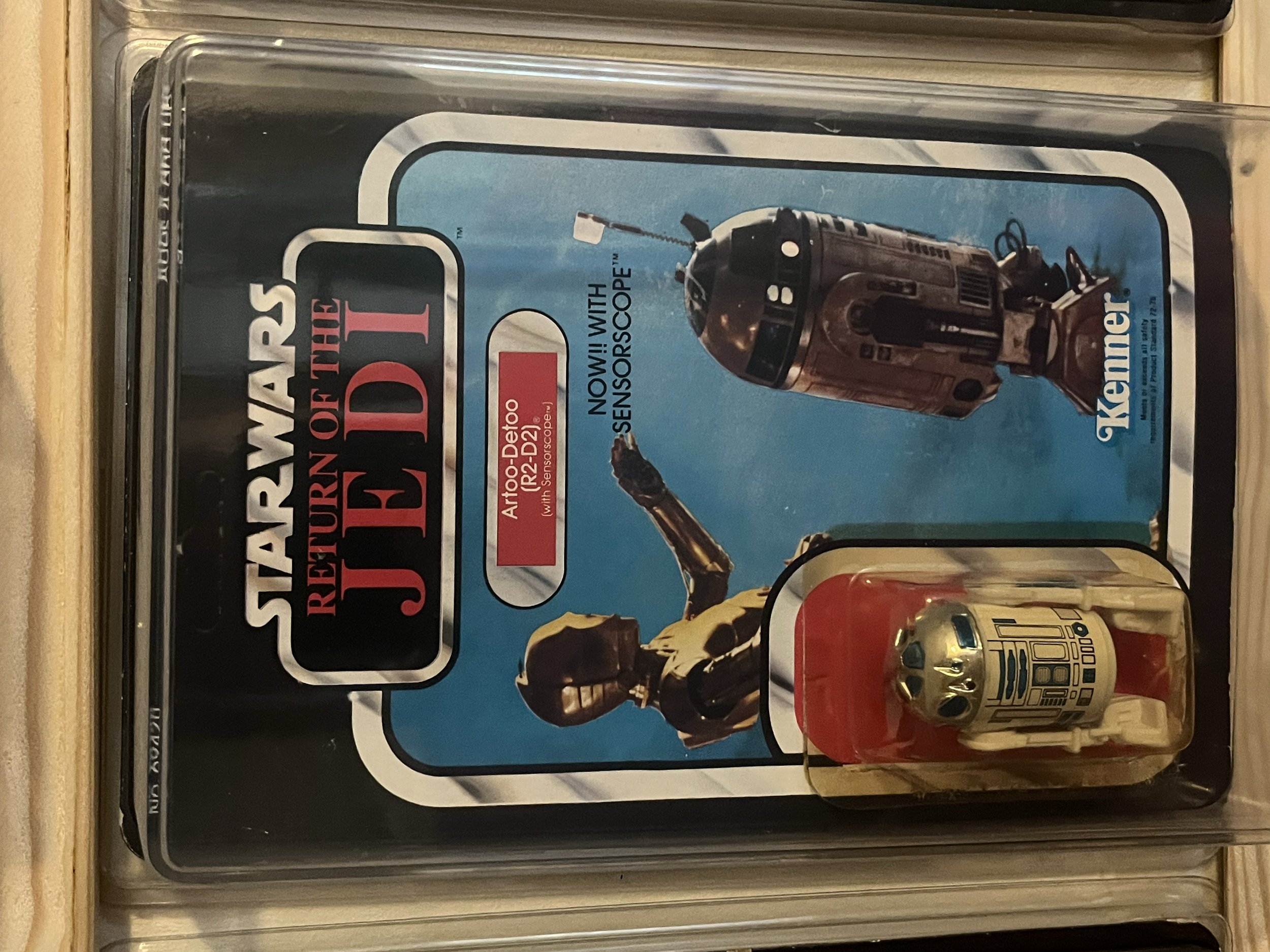 Star Wars Star Wars: The Empire Strikes Back action figure set in clear plastic packaging, featuring a figure and a can with a robot design, on a wooden surface.