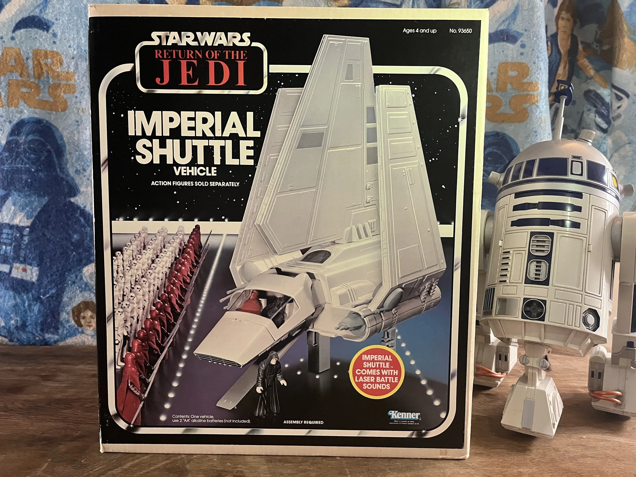 Star Wars Return of the Jedi Imperial Shuttle toy box with image of the shuttle and R2-D2 figure, on a blue surface with Star Wars-themed fabric background.