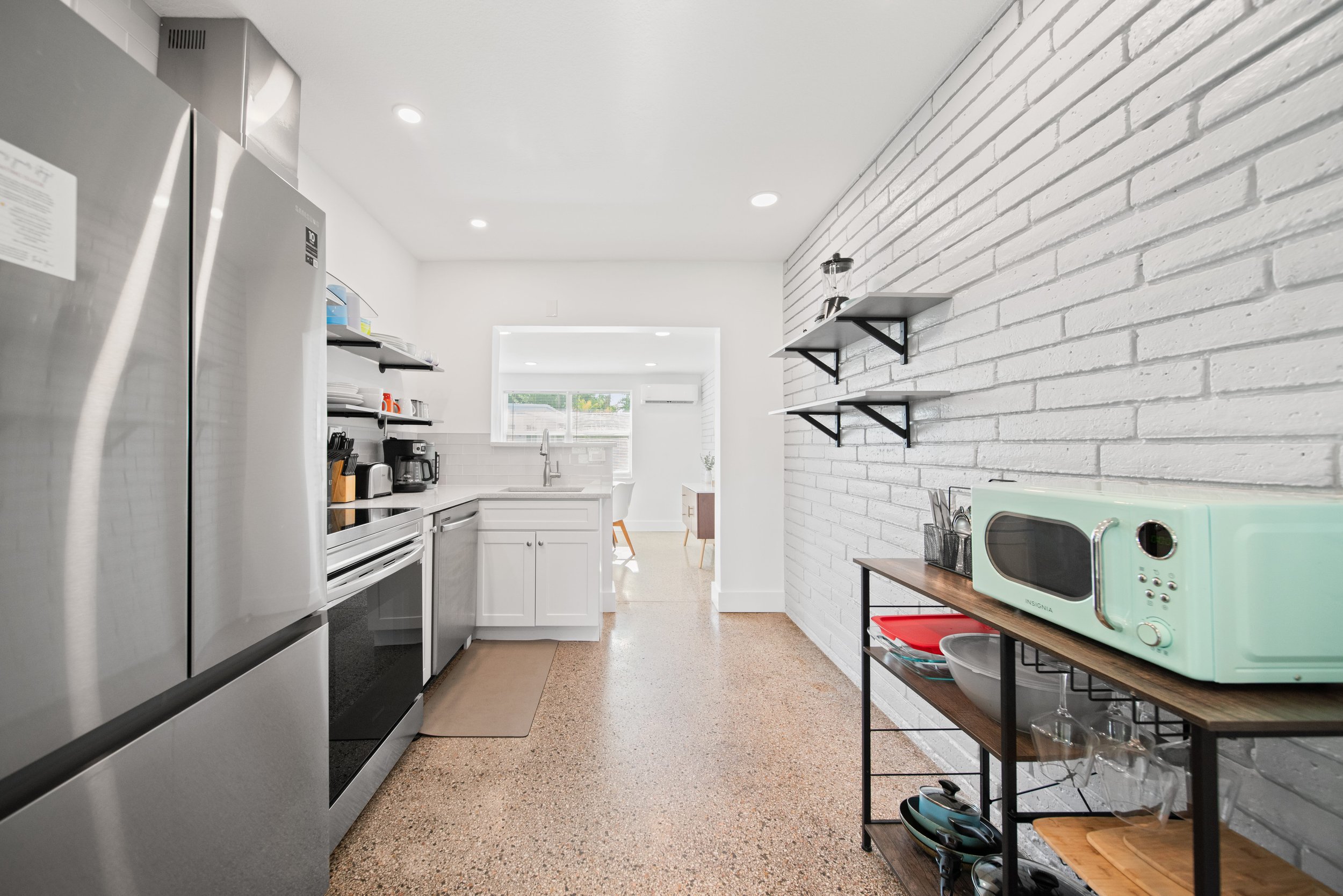 Modern kitchen with white cabinets, stainless steel appliances, and open shelving on white brick wall.