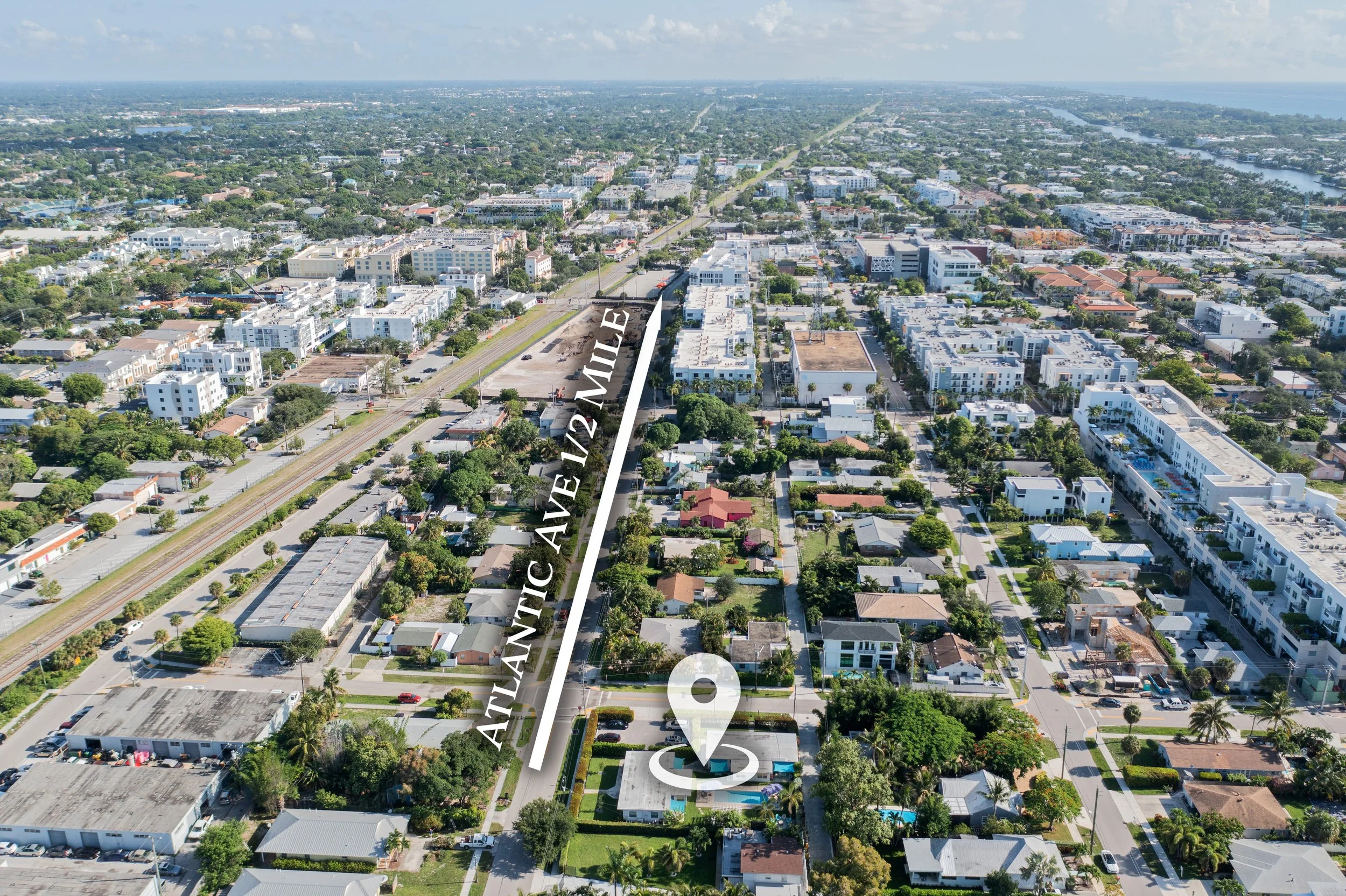 Aerial view of a city with residential and commercial buildings, streets, trees, waterways, and distant horizon under cloudy sky.