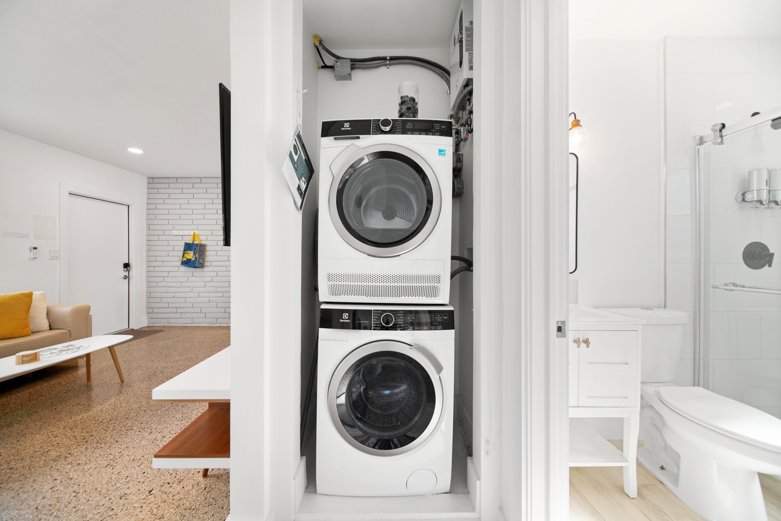 Stacked washer and dryer in a laundry closet next to a bathroom with a shower.