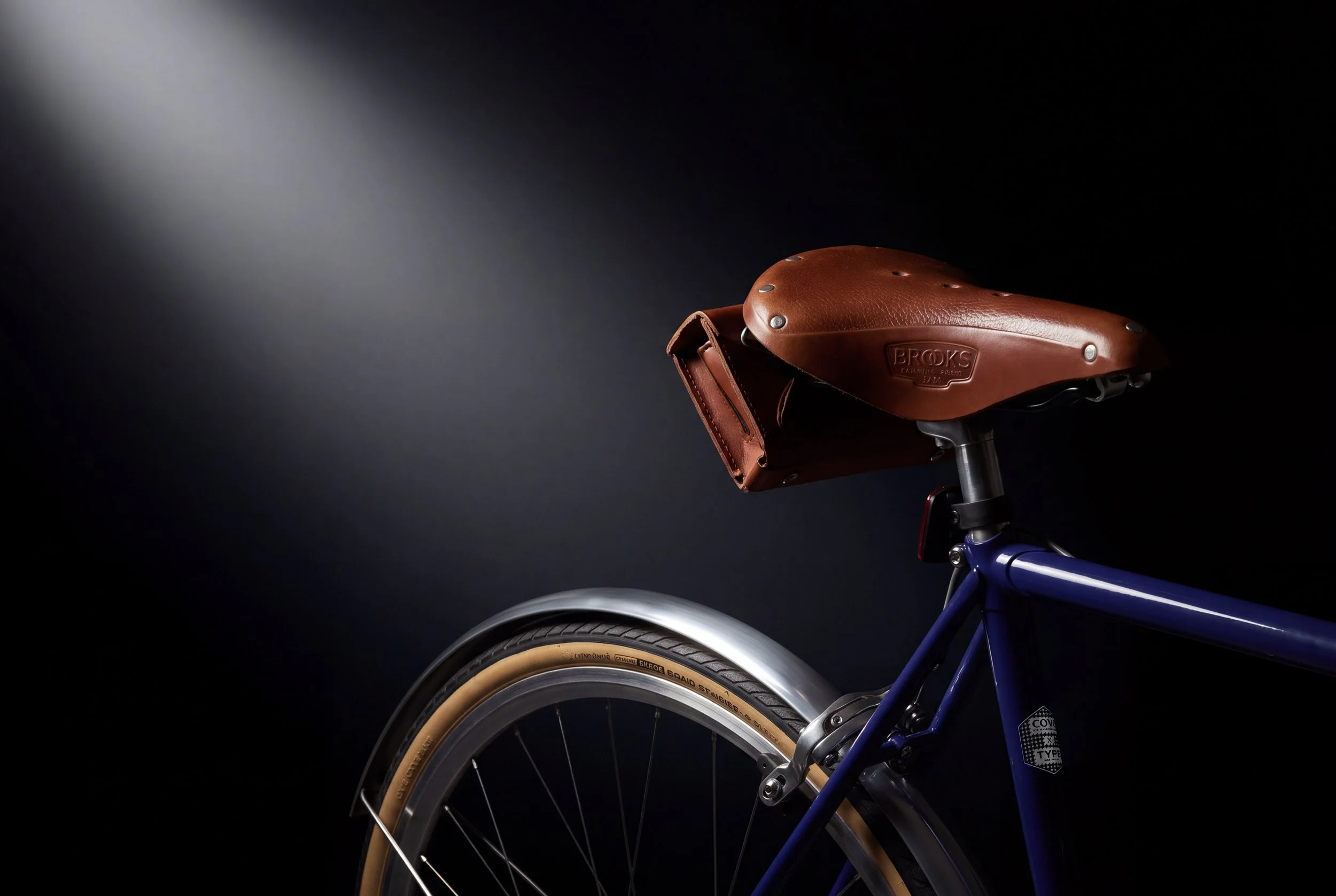Fahrradsattel aus braunem Leder auf einem blauen Fahrradrahmen, im Dunkeln beleuchtet
