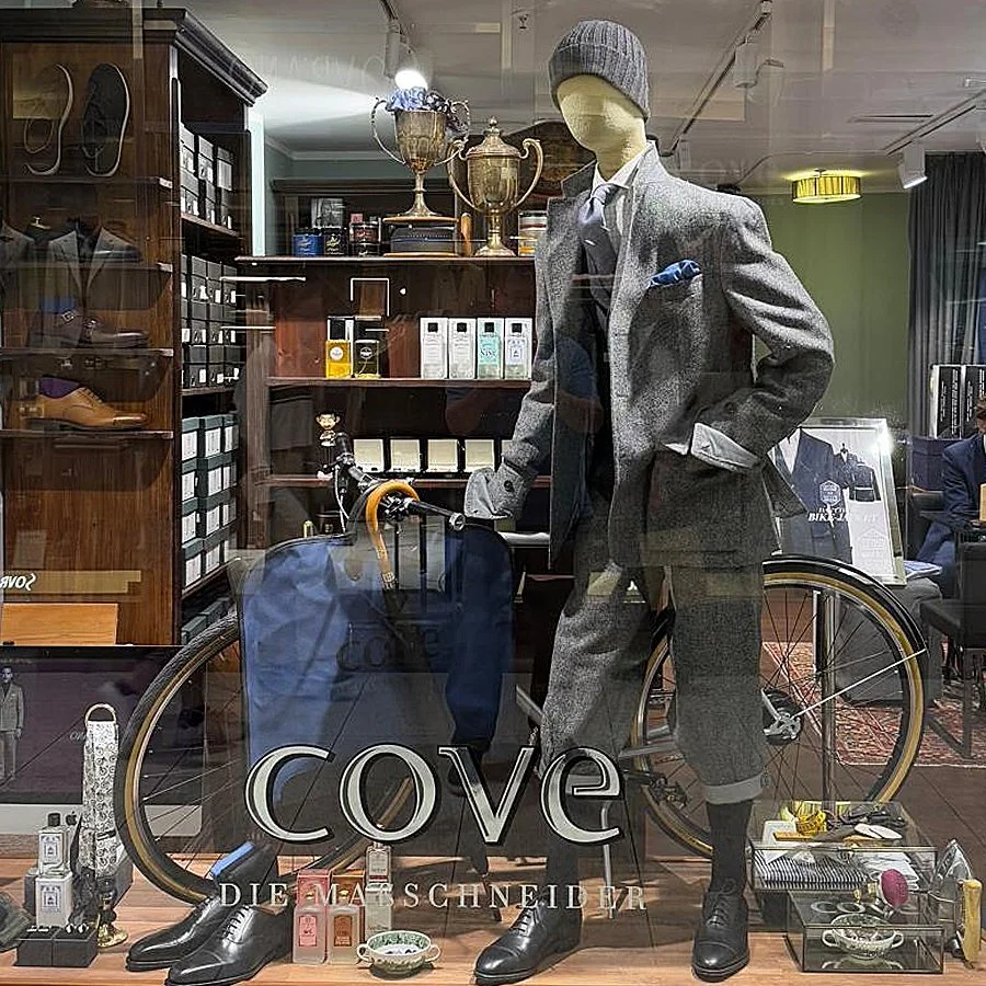 Schaufensterdisplay mit einem mannequinh after in einem Anzug mit Mütze, einem Fahrrad, mehreren Trophäen, Schuhen und Kosmetikprodukten in einem Möbelgeschäft.