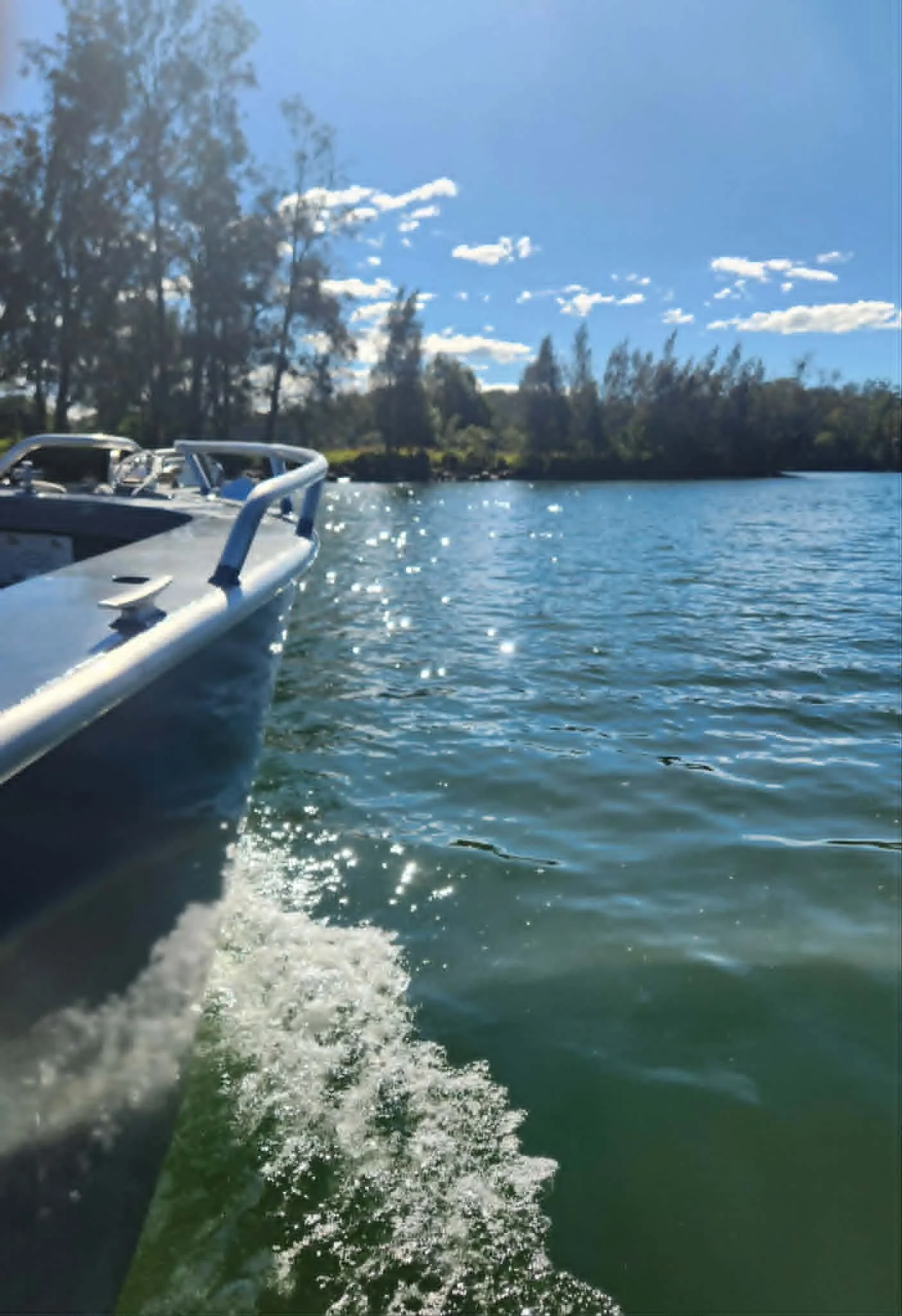 View of a boat on a lake or river with trees and blue sky in background. Water has a wake behind the boat.