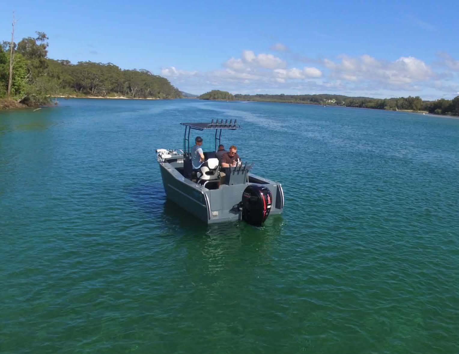 A boat with three people on a river under a blue sky with scattered clouds.