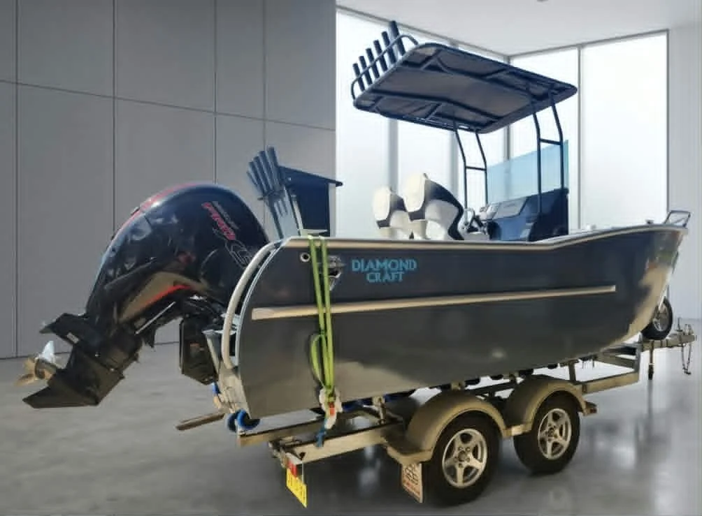 A small Black and white motorboat with a canopy, mounted on a double-axle trailer, inside a modern indoor space with large glass windows.