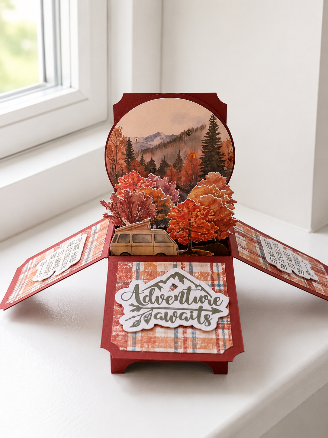 Three-dimensional pop-up camping scene inside a box with trees, mountains, a van, and the phrase 'Adventure awaits' on the front.