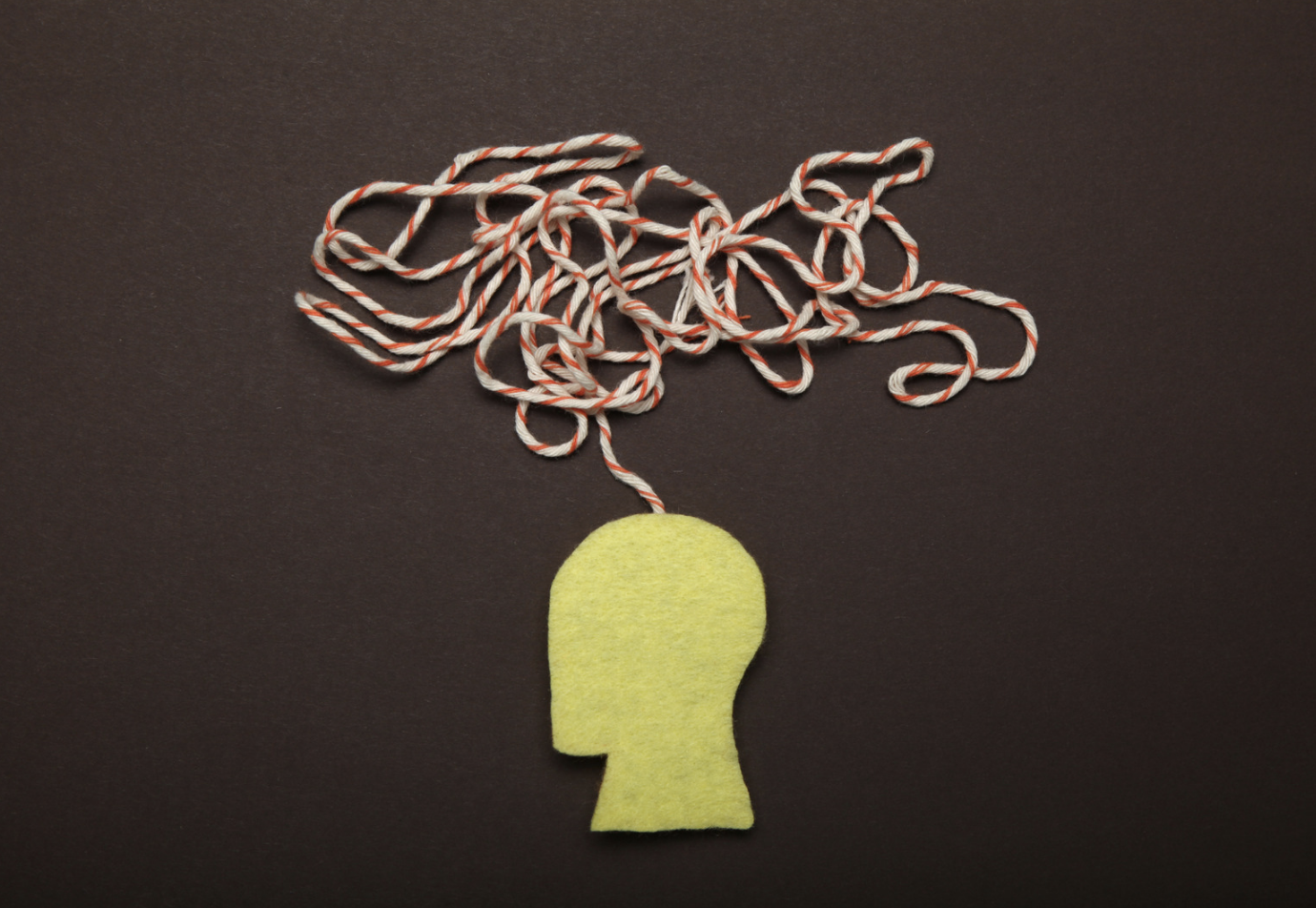 A yellow felt cutout of a human head silhouette with red and white striped string tangled above it on a black background.