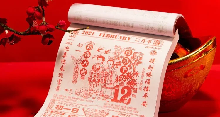 Red calendar page for February 2021 with Chinese lunar New Year illustrations, red flowers, and a gold bowl placed on a red surface.