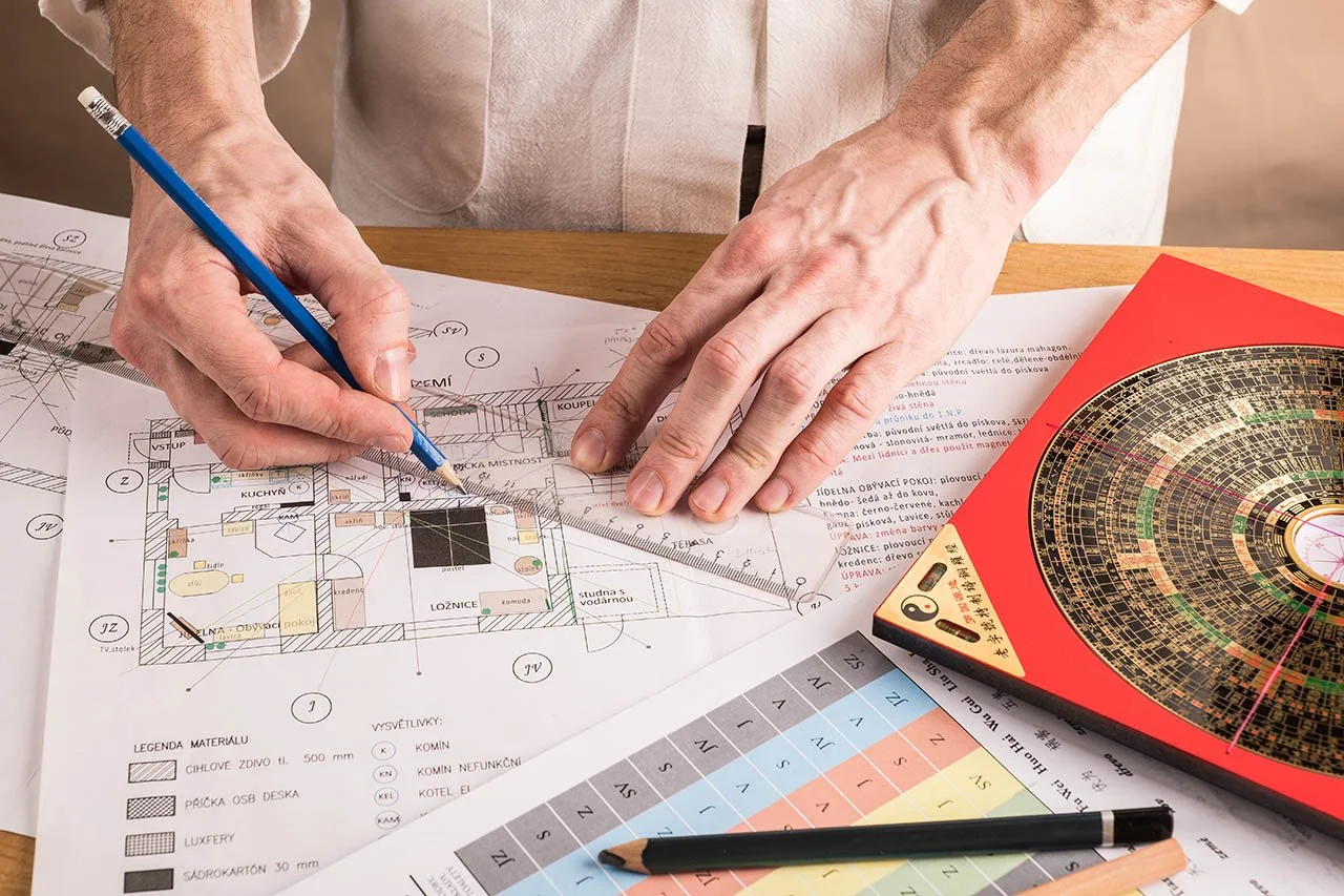 Person working on architectural plans or blueprint at a desk, with a colorful paper circle, color chart, pen, and ruler.
