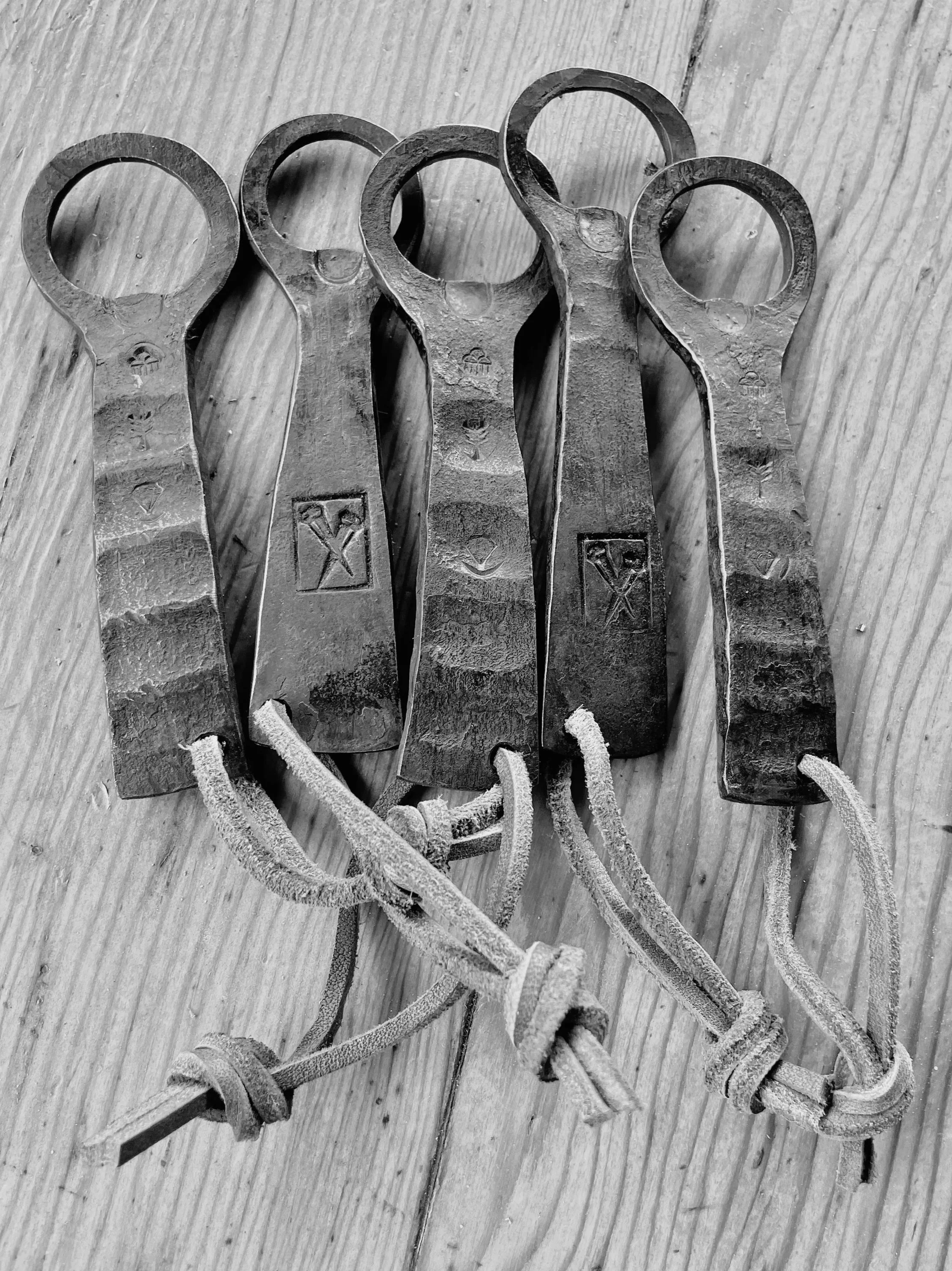 A set of rusty metal bottle openers with tied leather loops on a wooden surface.