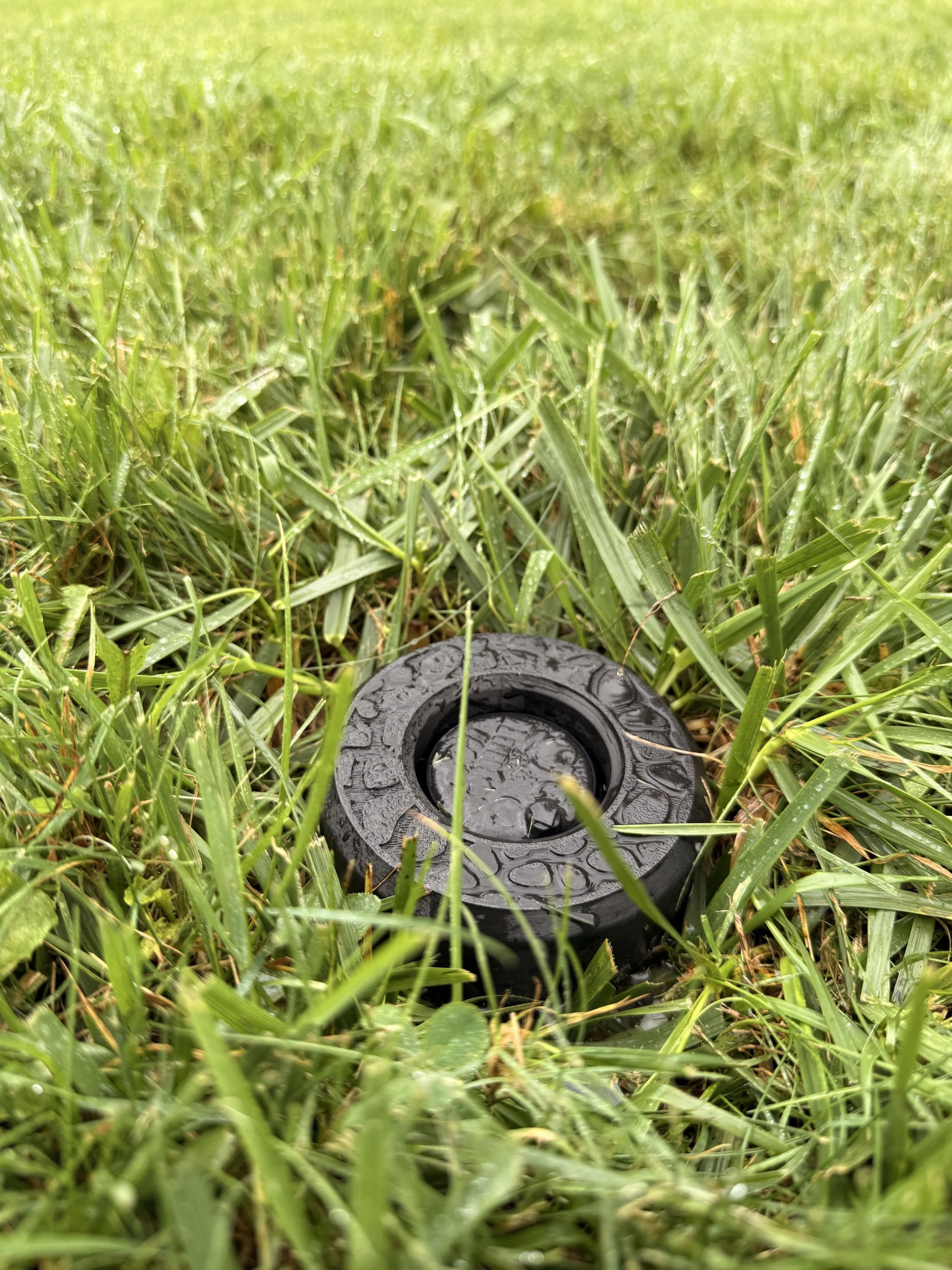 Black IngenioTech Full Guard fitted around a sprinkler rotor, surrounded by lawn grass.