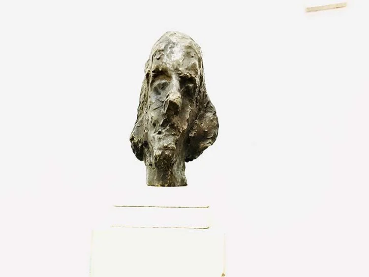 Close-up of an abstract, rough sculpture of a human head's facing front, bronze, 25 cm, 2014