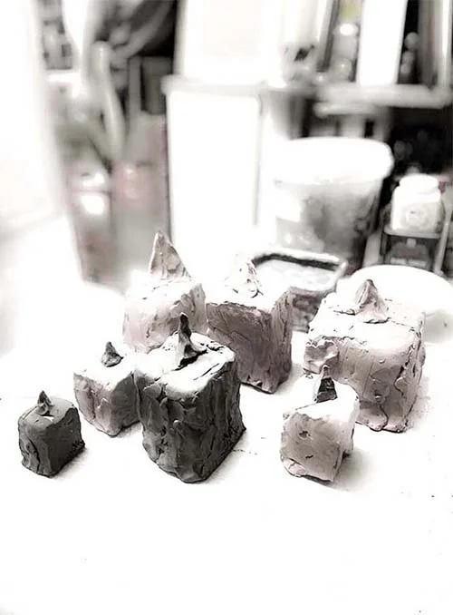 Close-up of four small, irregularly shaped pyramid sculptures with pointed tops, placed on a flat surface against a white background, 2023