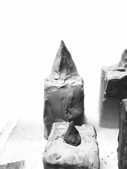 Close-up of four small, irregularly shaped pyramid sculptures with pointed tops, placed on a flat surface against a white background, 2023