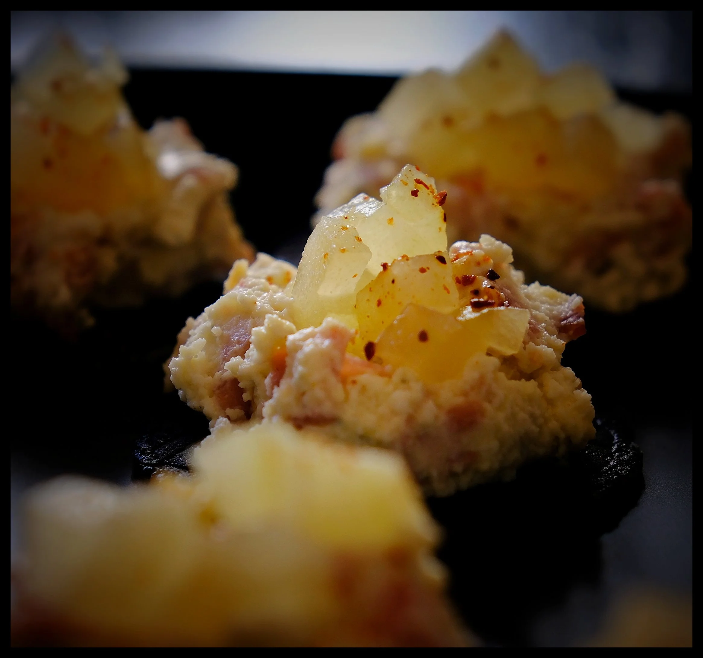 Close-up of a heap of mashed potatoes topped with red chili flakes on a black plate.