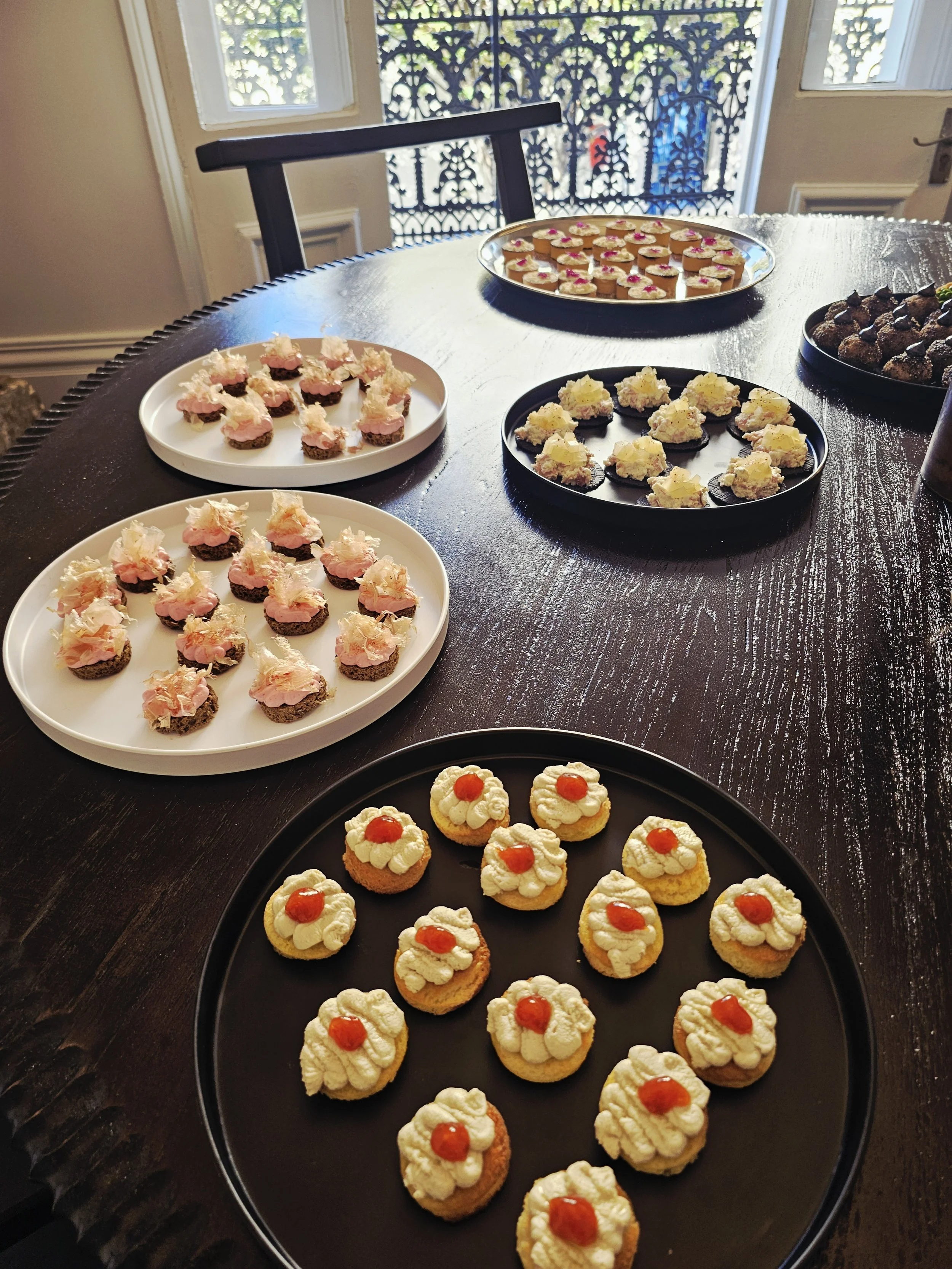 Various decorated cookies arranged on black and white trays on a wooden table, with a balcony and garden visible in the background.