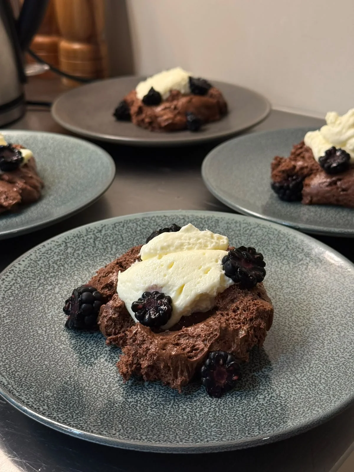 Chocolate blackberry dessert on a blue-gray plate with whipped cream topping.