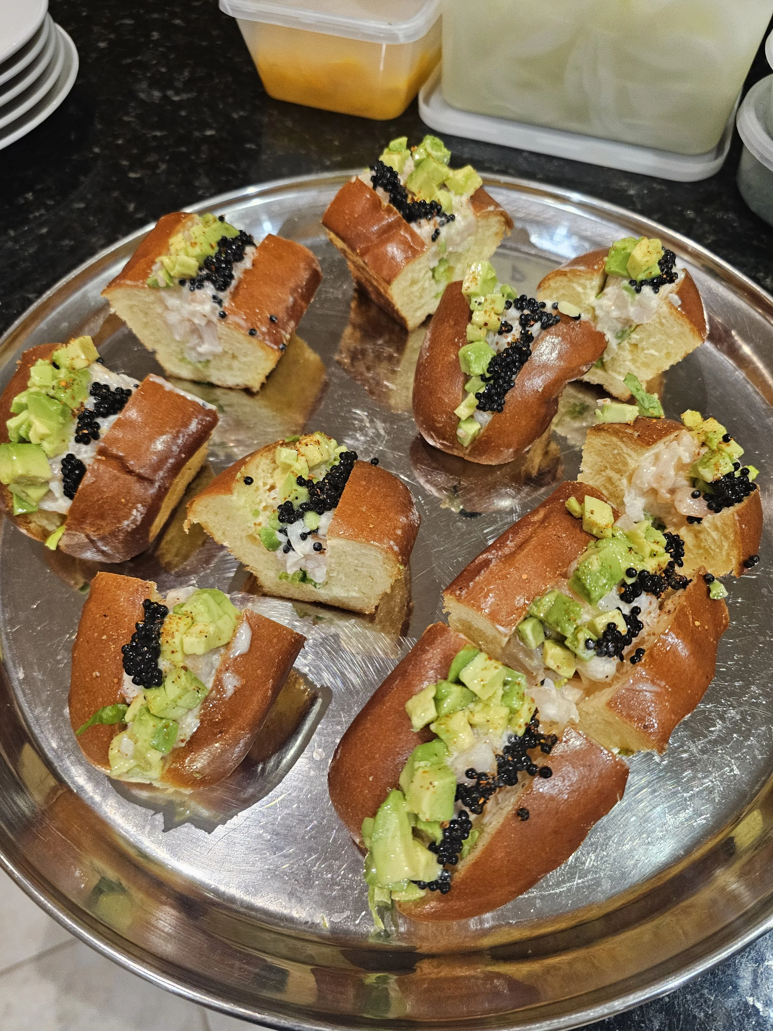Several pieces of bread filled with seafood and topped with diced avocado and black caviar on a silver tray.