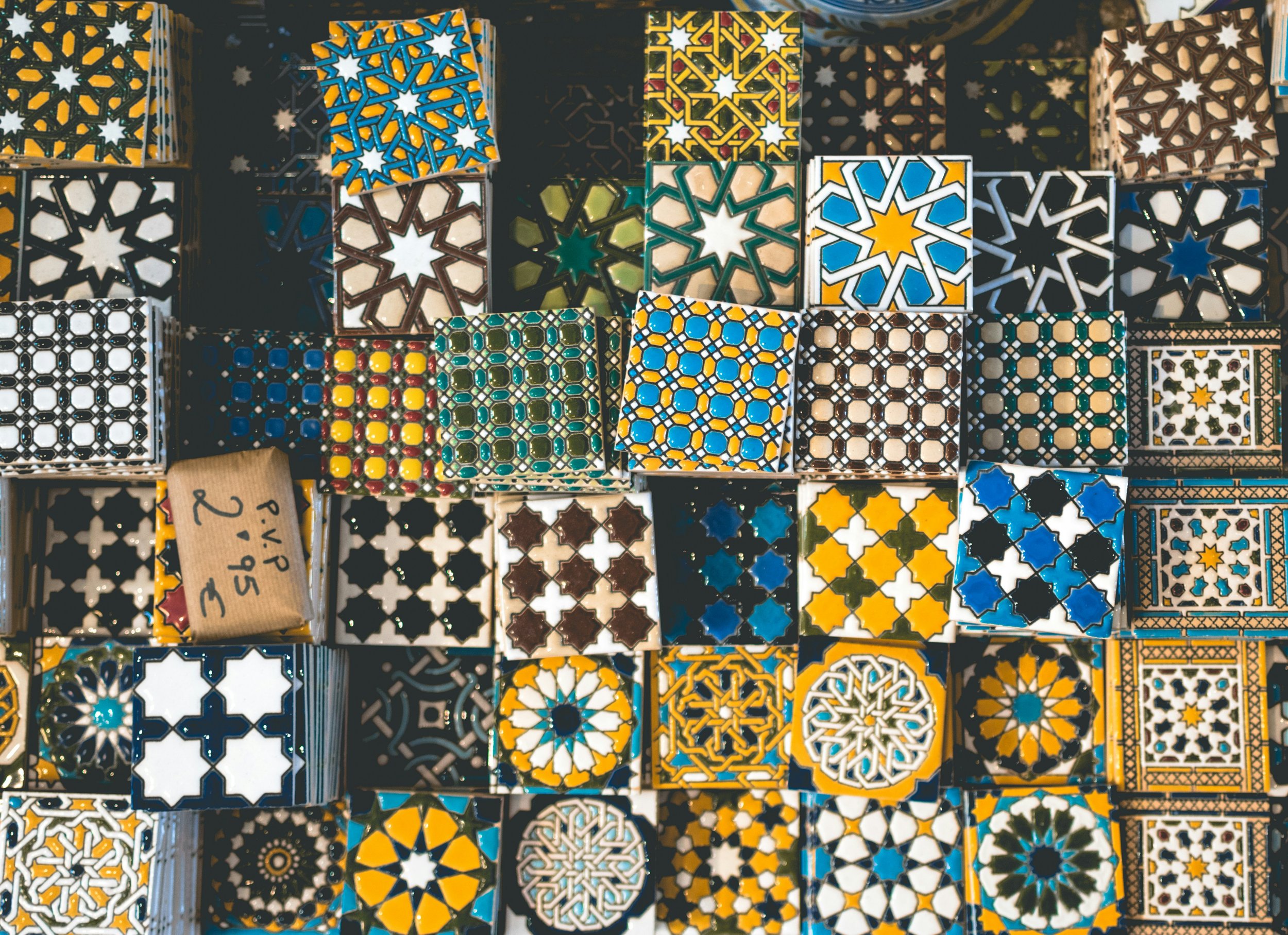 Colorful mosaic tiles with geometric patterns in various shapes and colors, including blue, yellow, white, black, and green, arranged in rows.