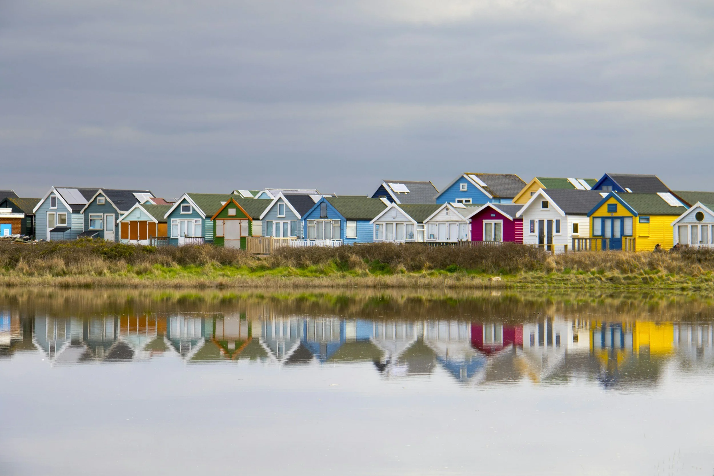 Colorful houses with various painted exteriors, including blue, yellow, white, and green, situated along water with a cloudy sky above.