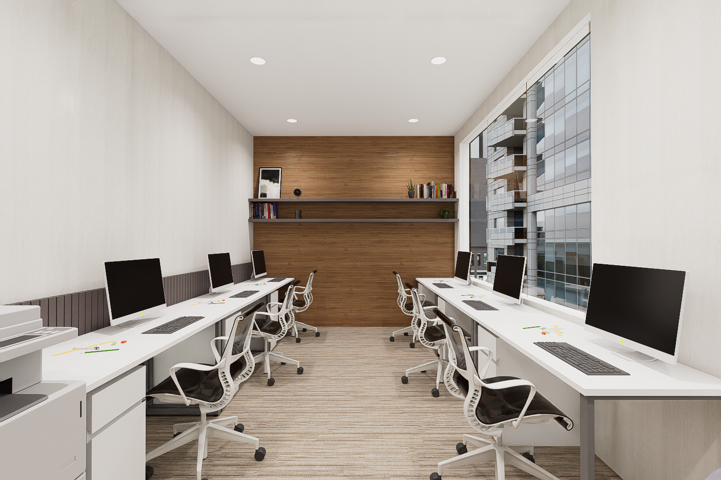 Empty modern office with row of desks and computers along windows, wooden accent wall at the back, and minimal decor.
