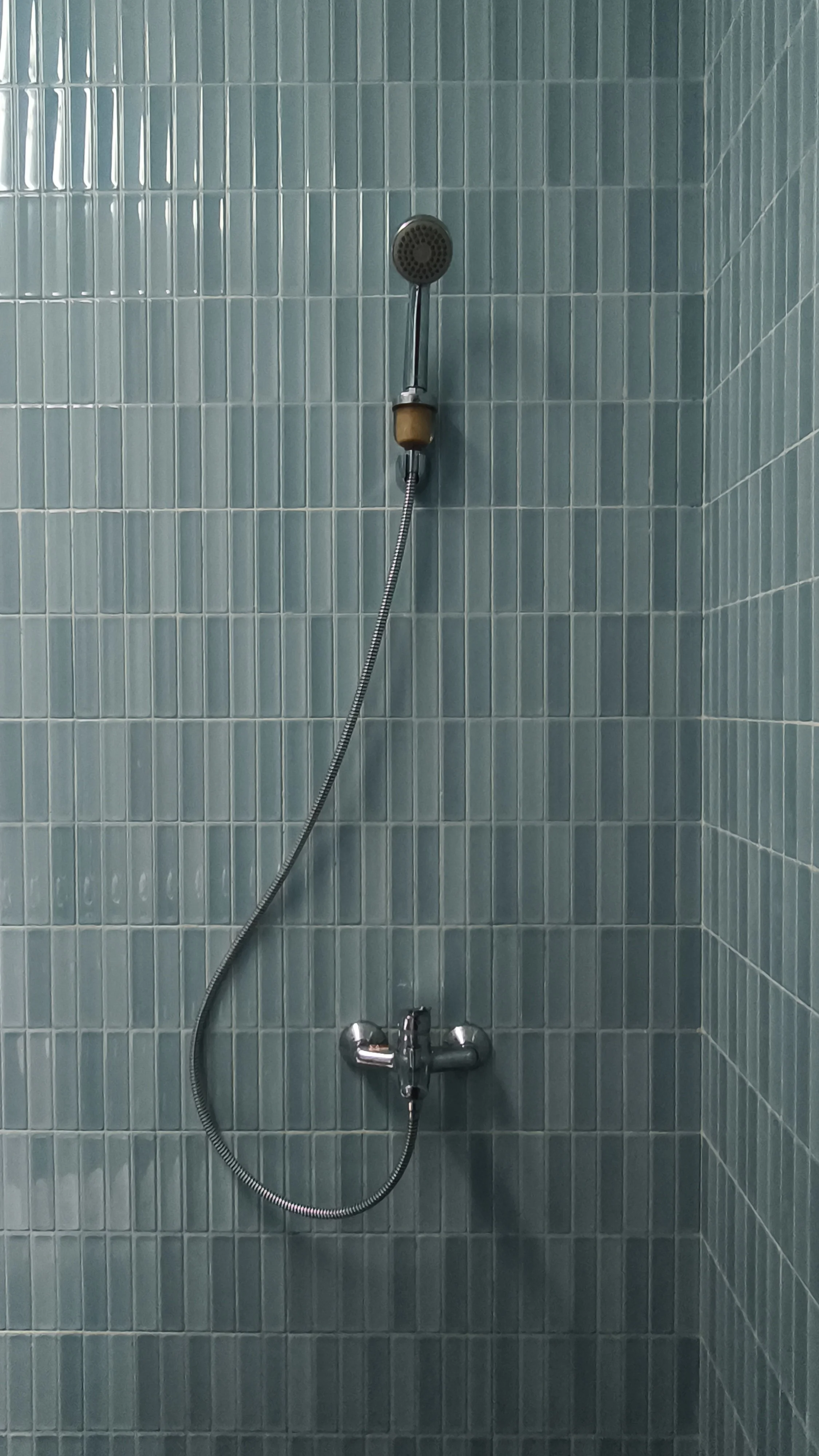 Shower with green tiles, showerhead on a metal rod, and a flexible shower hose connected to a mixer faucet.