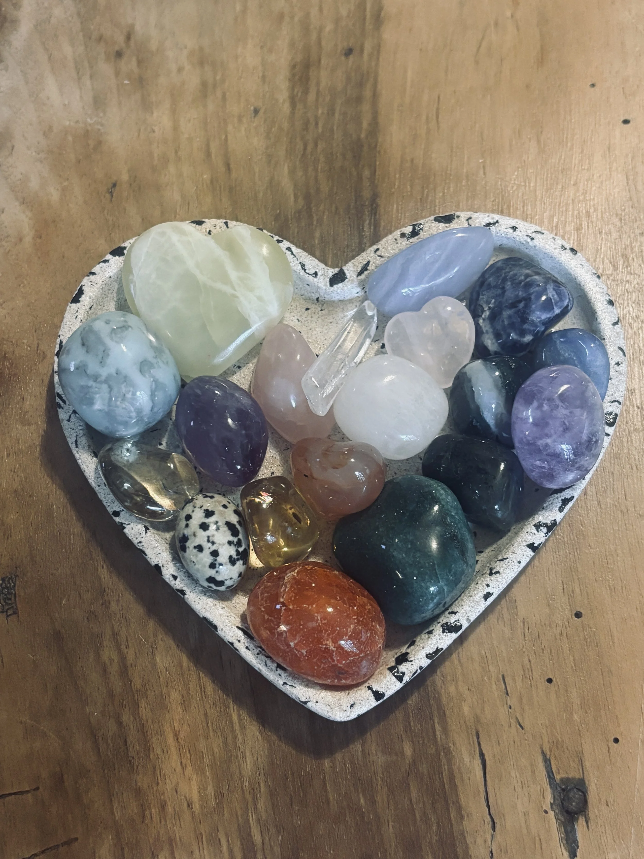 Un plateau en forme de cœur avec différents cailloux de couleurs variées et formes diverses, posé sur une surface en bois.