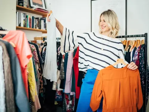 A woman dressed in pink standing in a clothing store with a pink counter, books, and colorful clothes hanging in the background