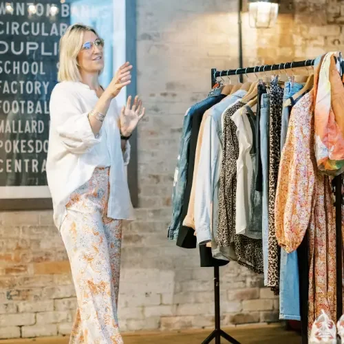 Woman shopping for clothes in a boutique, looking at a rack of assorted garments.