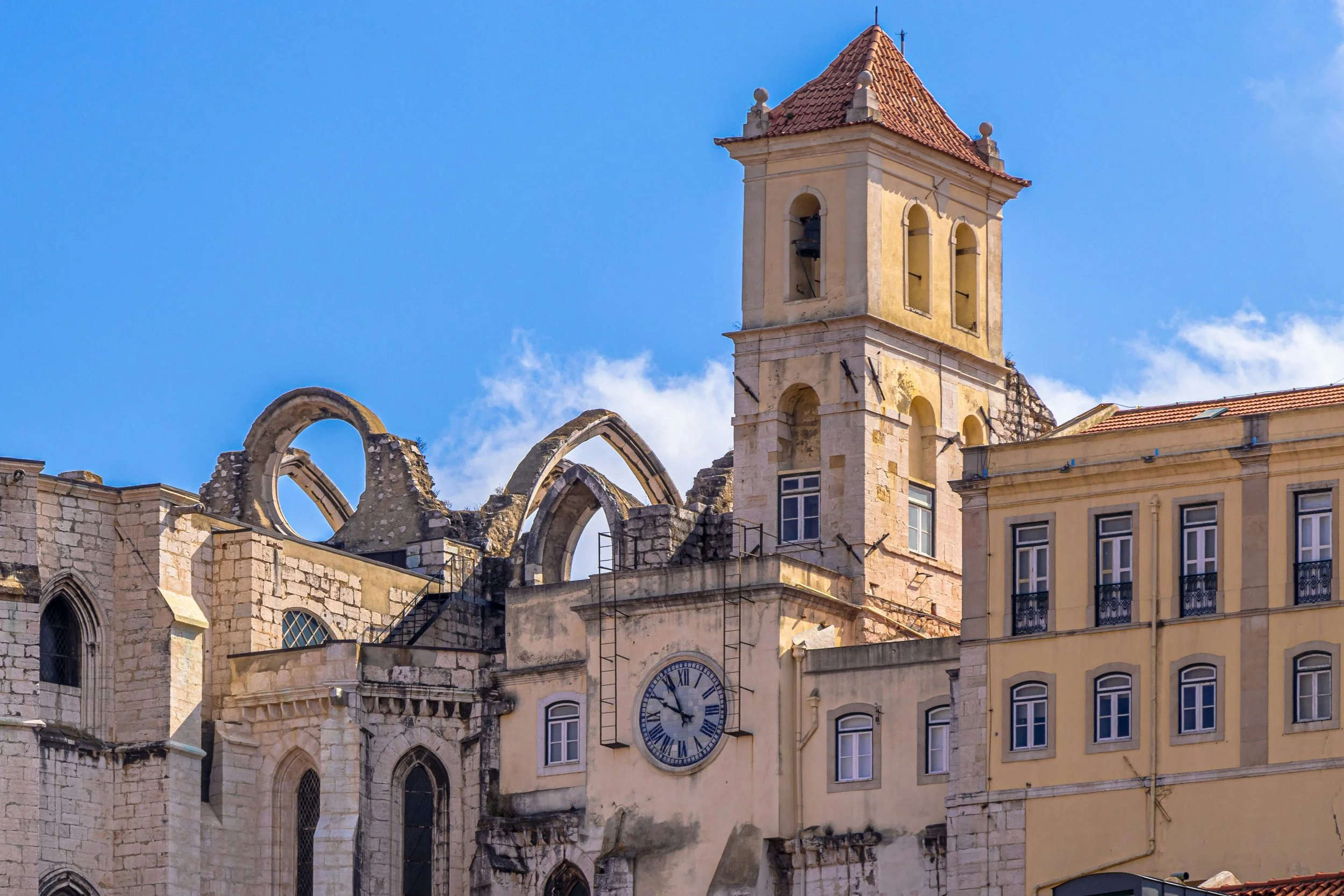 A historic building with a clock tower and bell, partially in ruins, under a blue sky with some clouds.