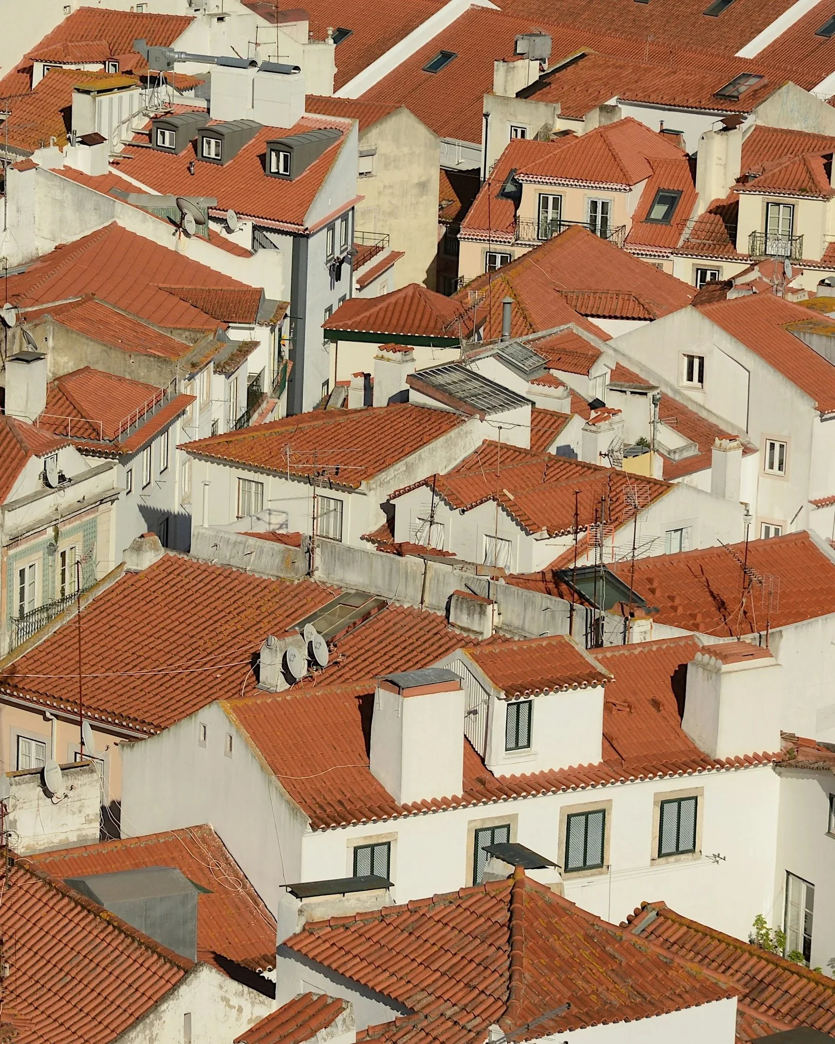 Aerial view of a dense cluster of buildings with red-tiled roofs, various chimneys, satellite dishes, and small windows.