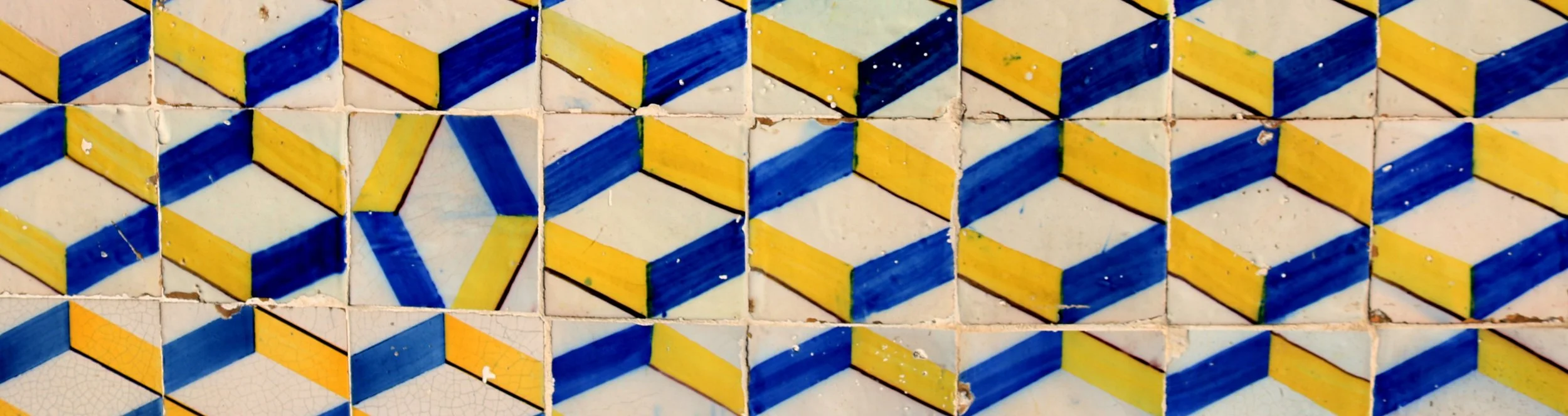 Close-up view of decorative mosaic tile wall featuring geometric cube patterns in blue, yellow, and white colors.