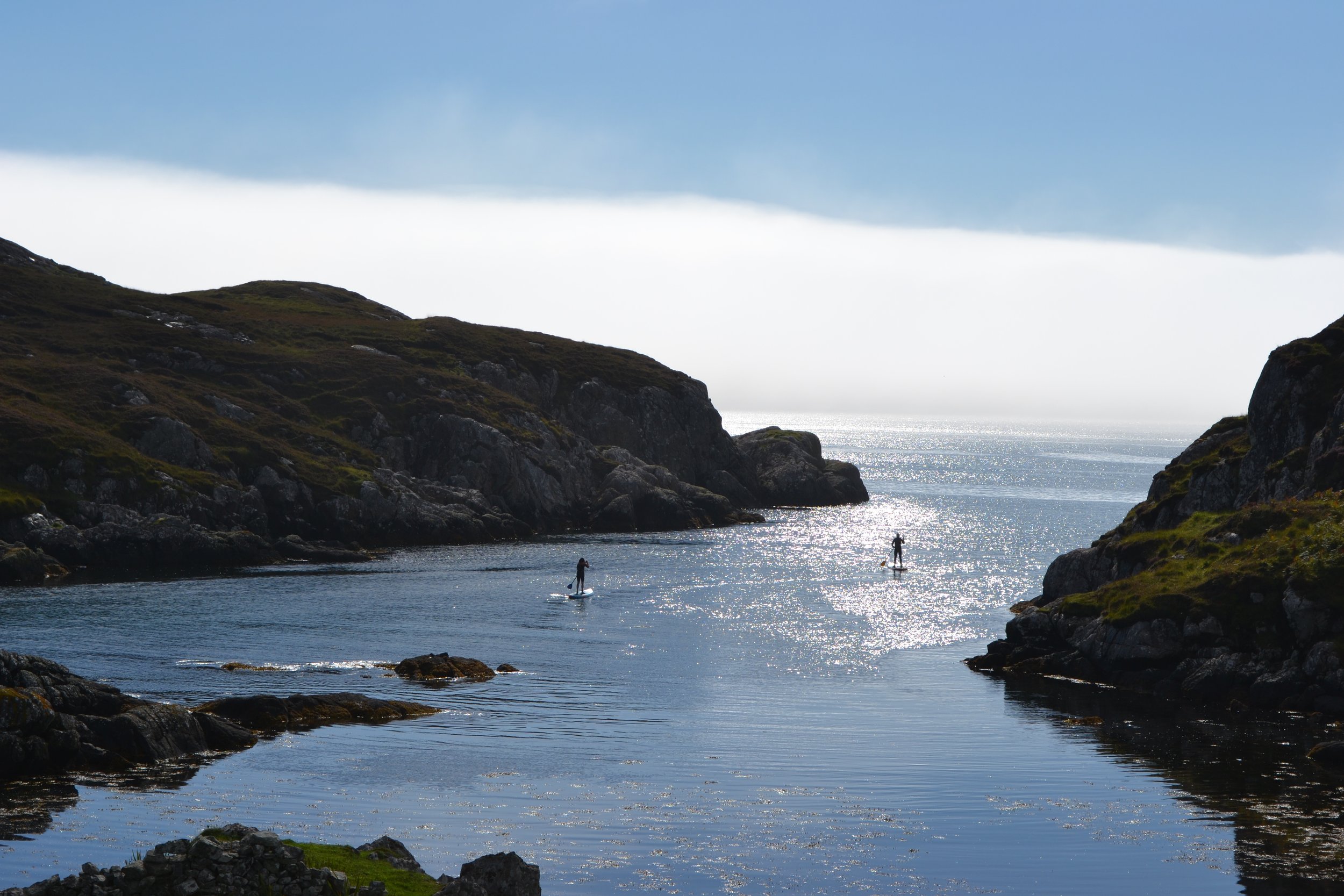 Coastal landscape with cliffs, water, and three people paddleboarding on a sunny day